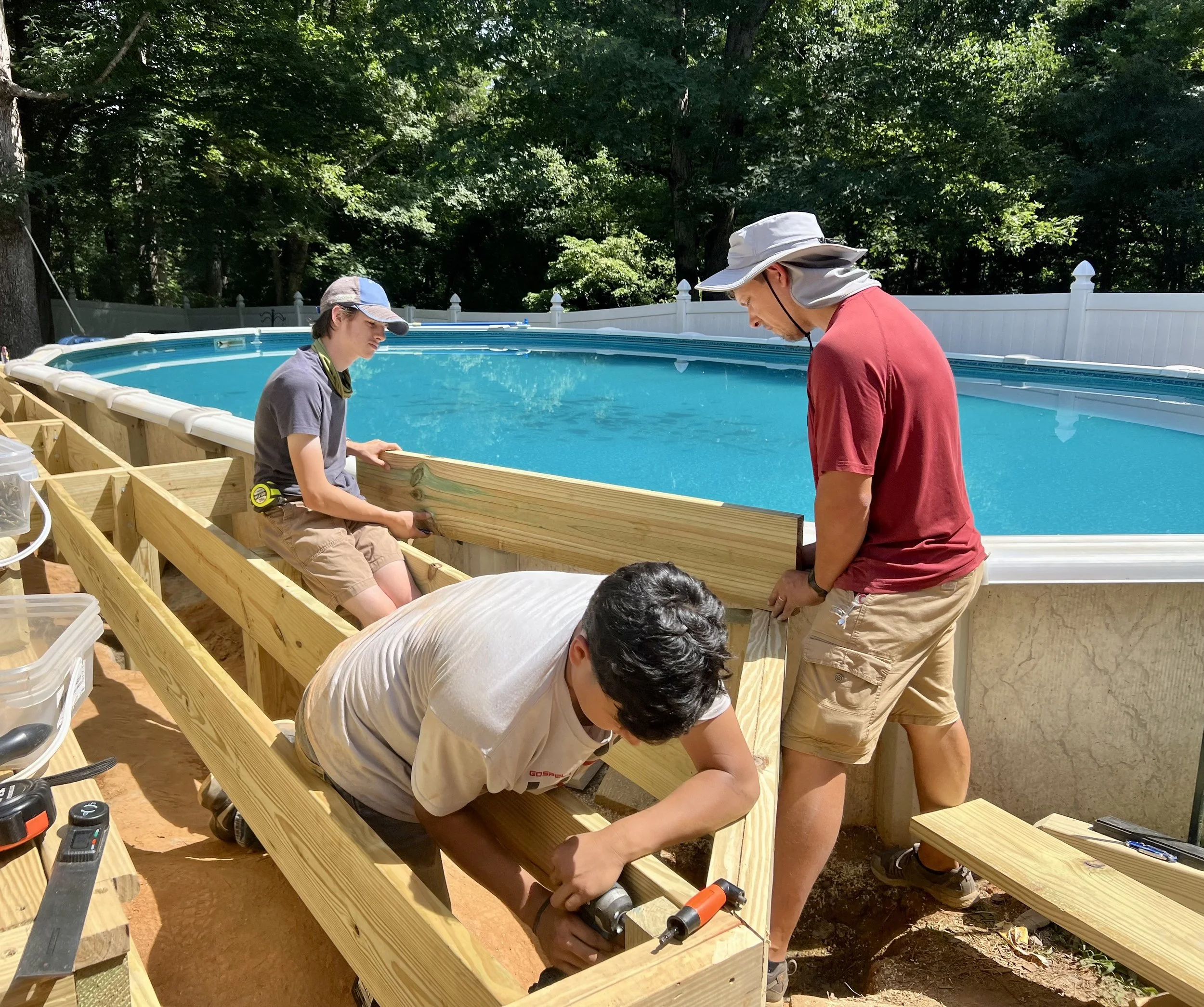 People building a wooden frame around an above-ground swimming pool.