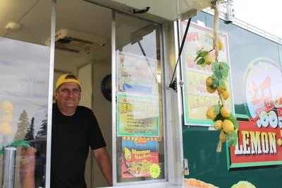 A man working at a lemon-flavored food truck decorated with lemons and a sign that reads 'Lemon'.
