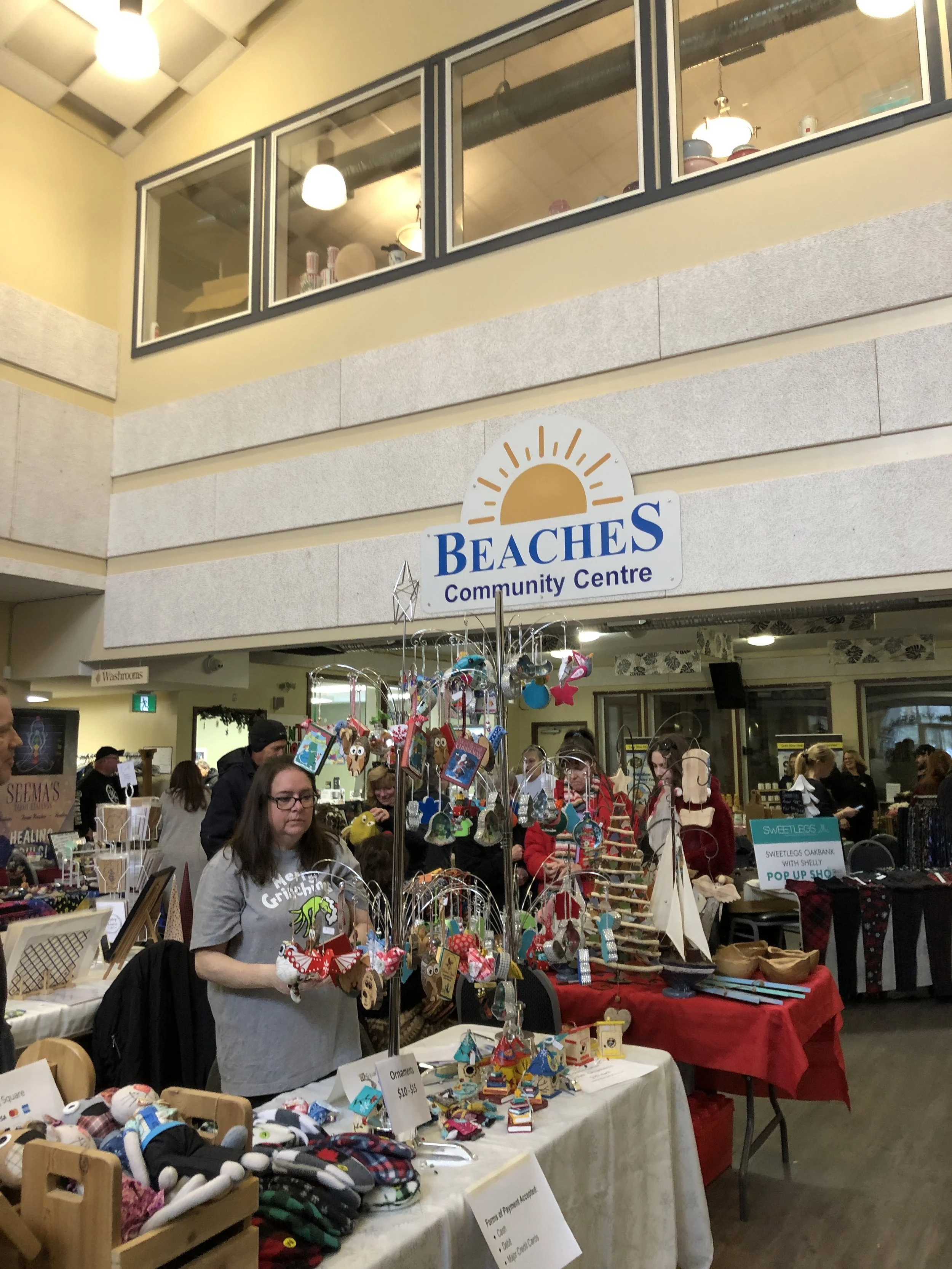 Indoor marketplace at Beache's Community Centre with vendors selling crafts, ornaments, and accessories, and people browsing items.