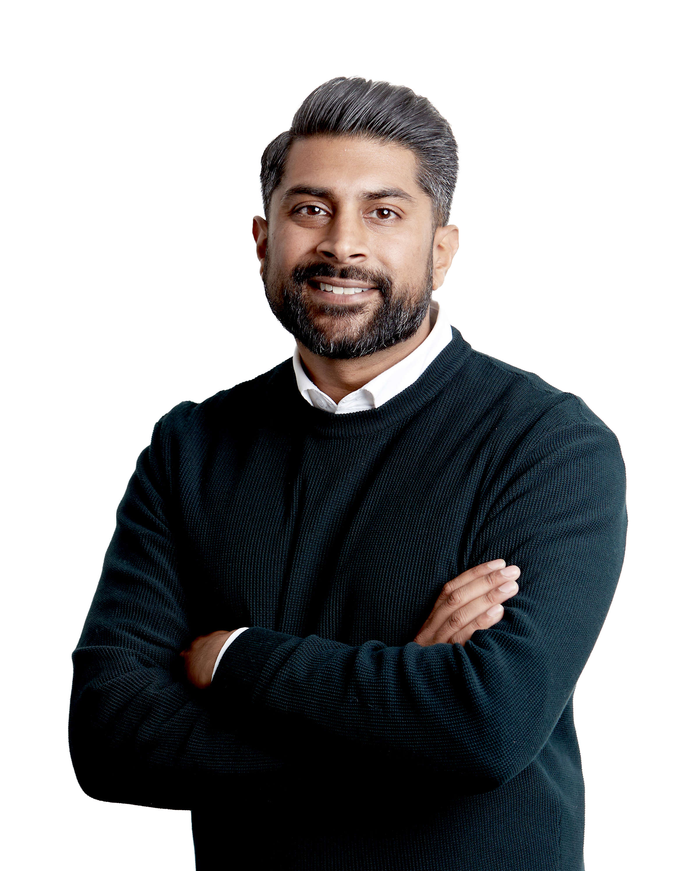 A man with dark hair, a beard, and a mustache smiling, wearing a black sweater over a white collared shirt with arms crossed.