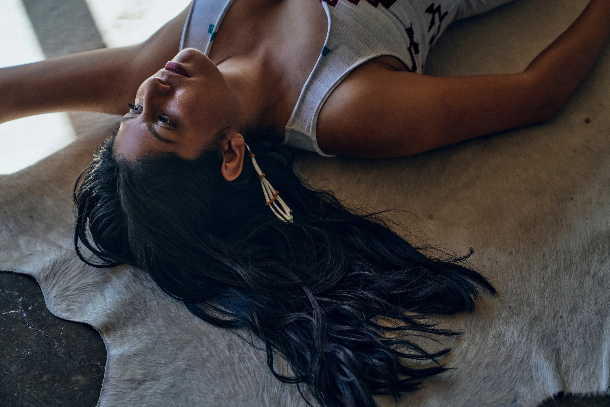A woman with long black hair lying on a cowhide rug, looking to the side.