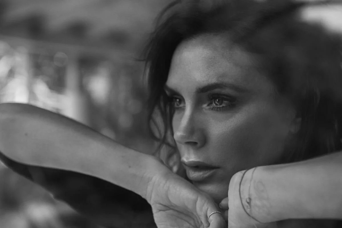 Close-up black and white photo of a woman with intense expression, resting her arm on her shoulders.