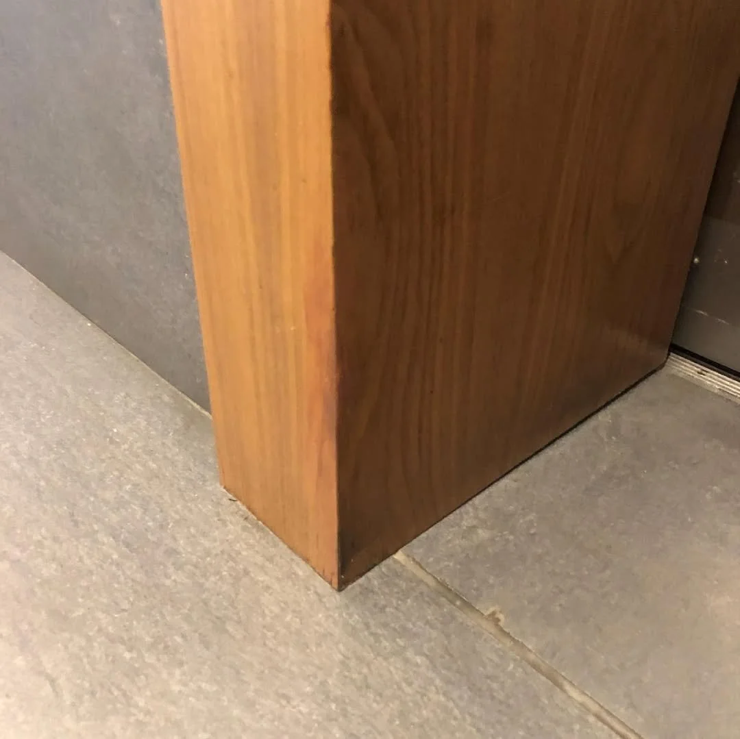Close-up of the corner of a wooden panel next to tiled flooring and a metal surface.