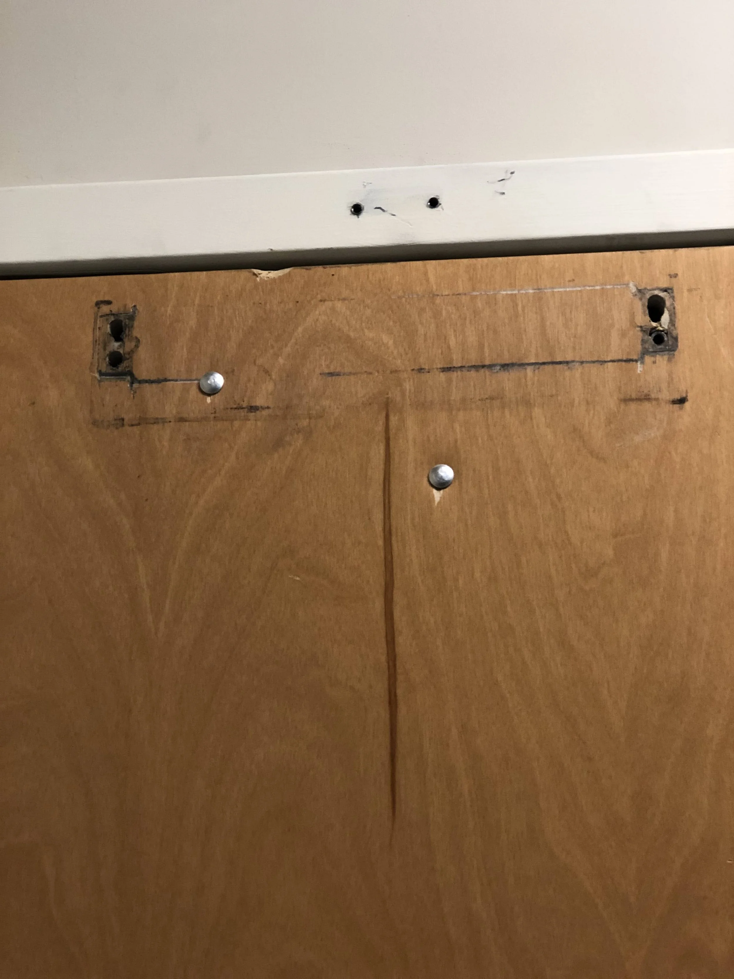 Part of a wooden cabinet with two metal screws and a scratch or opening in the wood, below a white section with three small holes and some scratches.