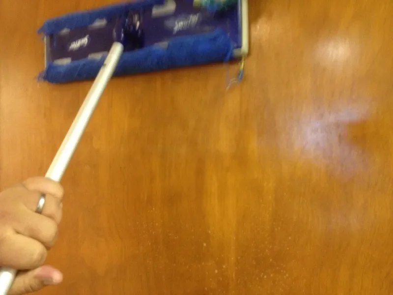 Person using a mop to clean a wooden floor or surface.