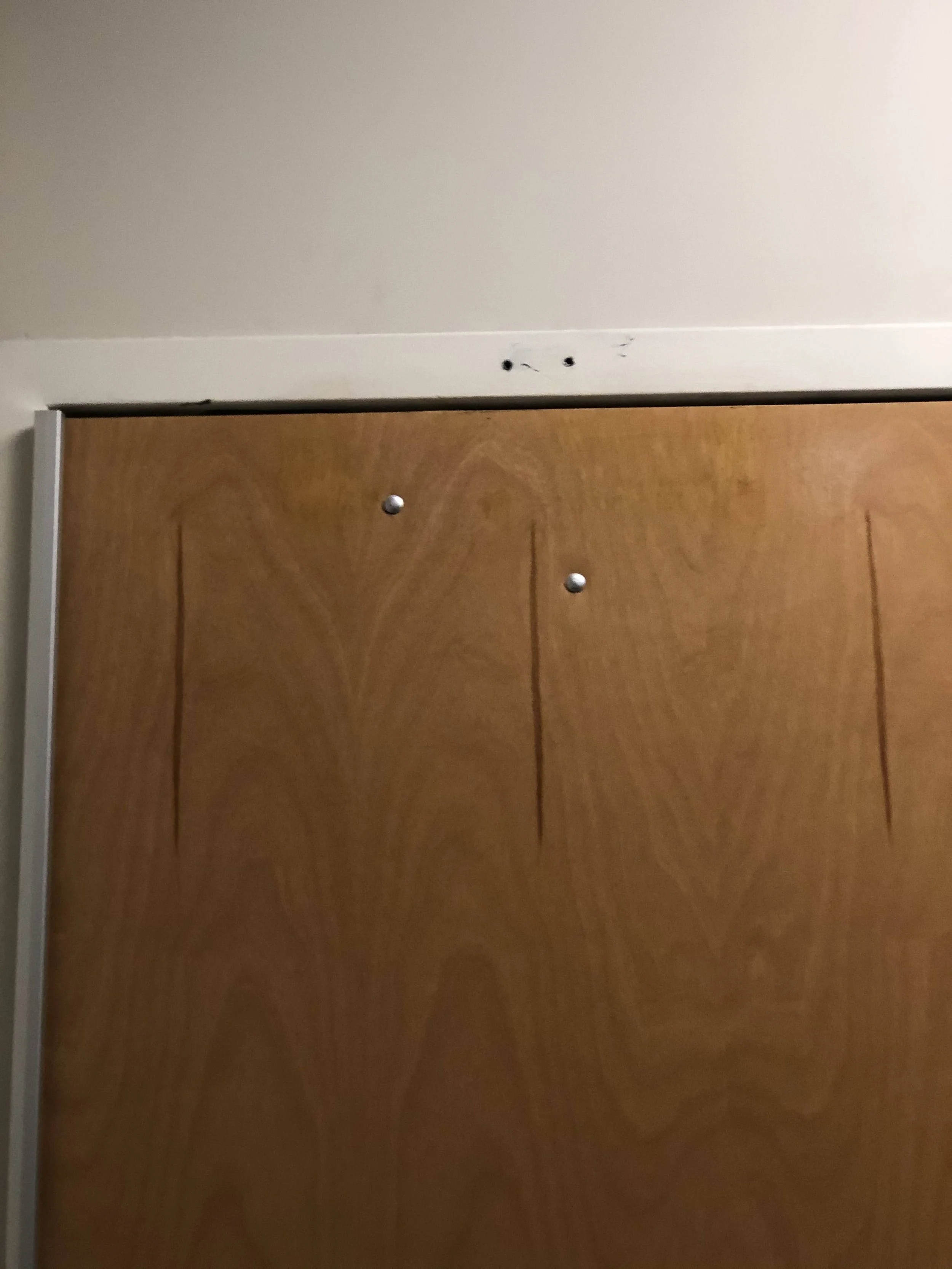Top part of a wooden closet door with three black marks on the white wall above it.