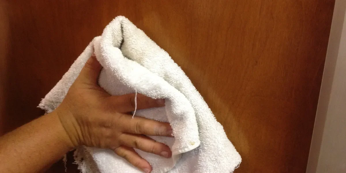 A person's hand wiping a wooden surface with a white towel.