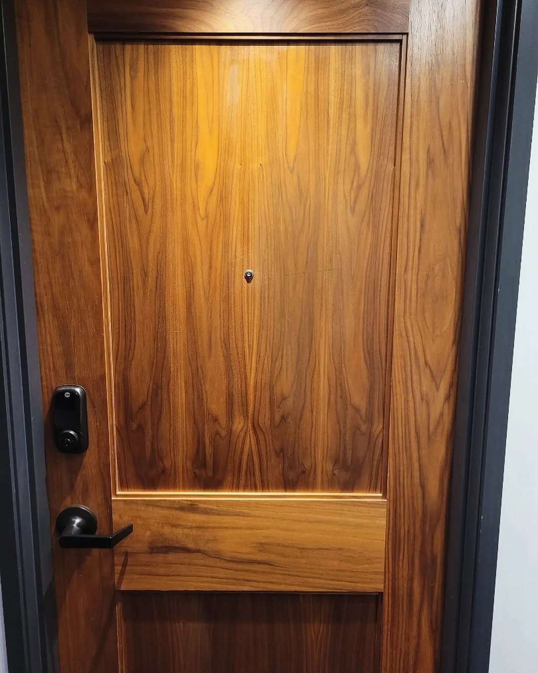 A wooden door with a peephole, a black electronic lock, and a black door handle.