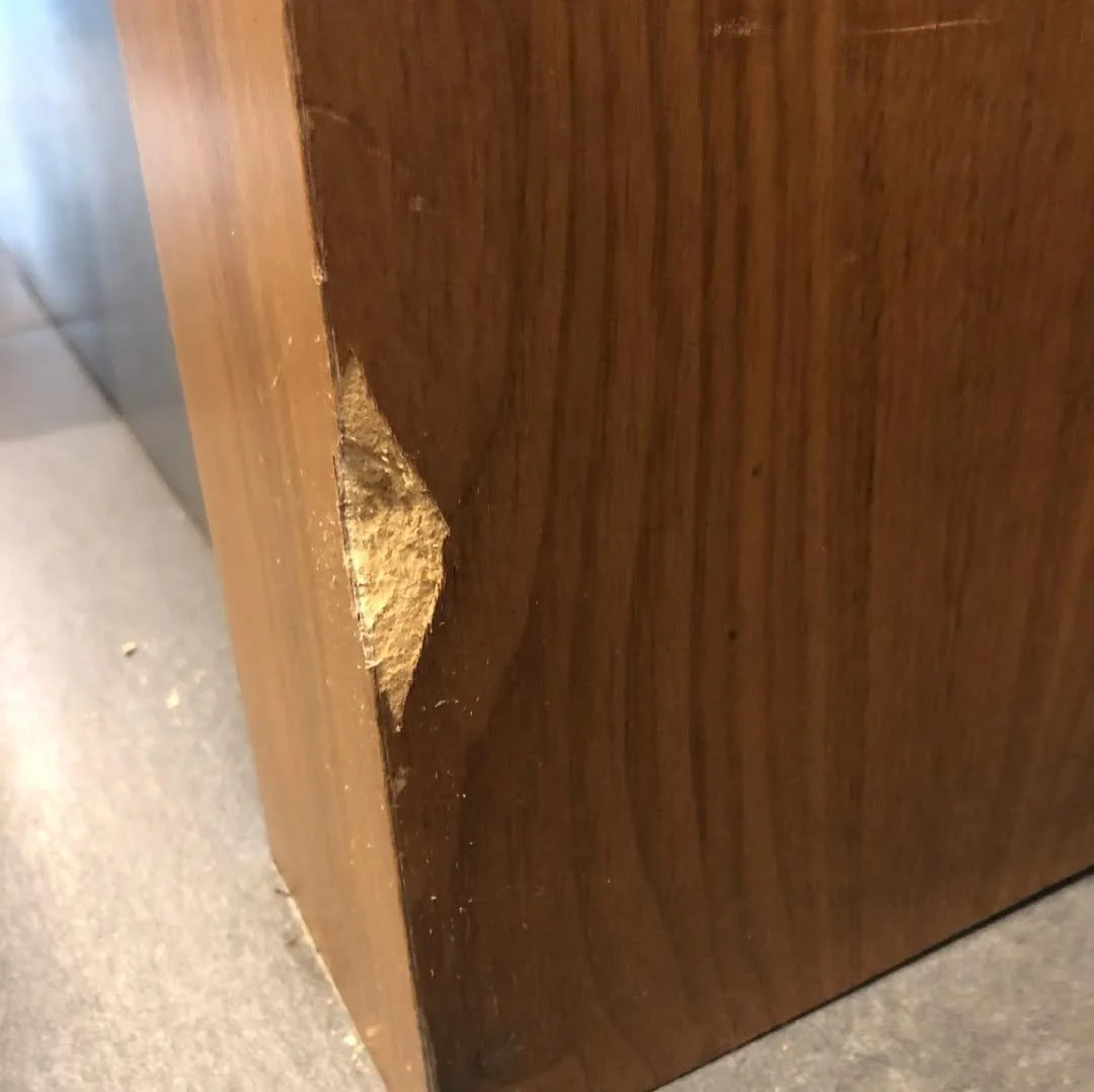 Close-up of damaged wooden furniture with peeling veneer and exposed fiberboard.