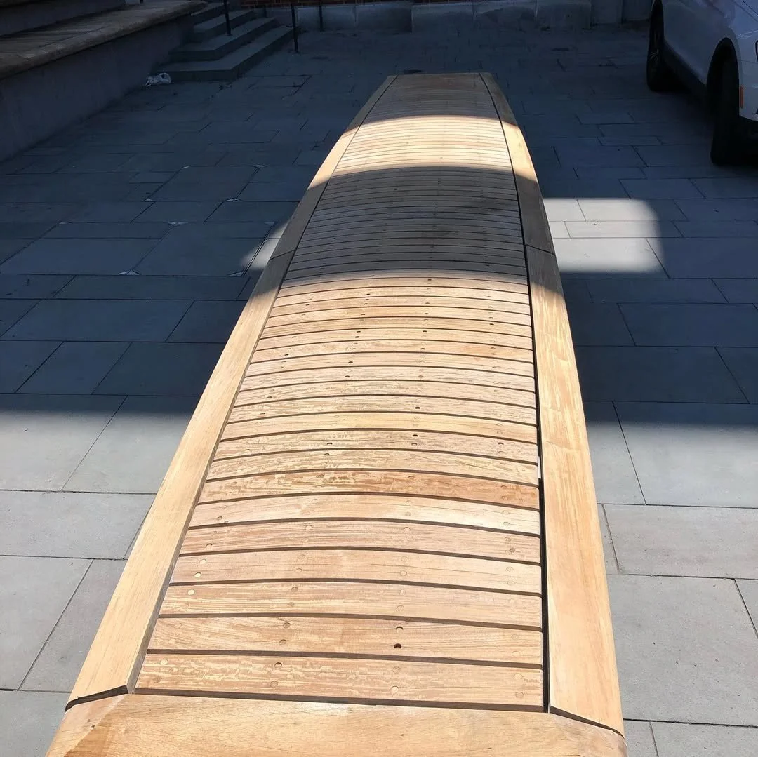 A wooden bench with a curved, slatted design, situated on a paved pavement outdoors.