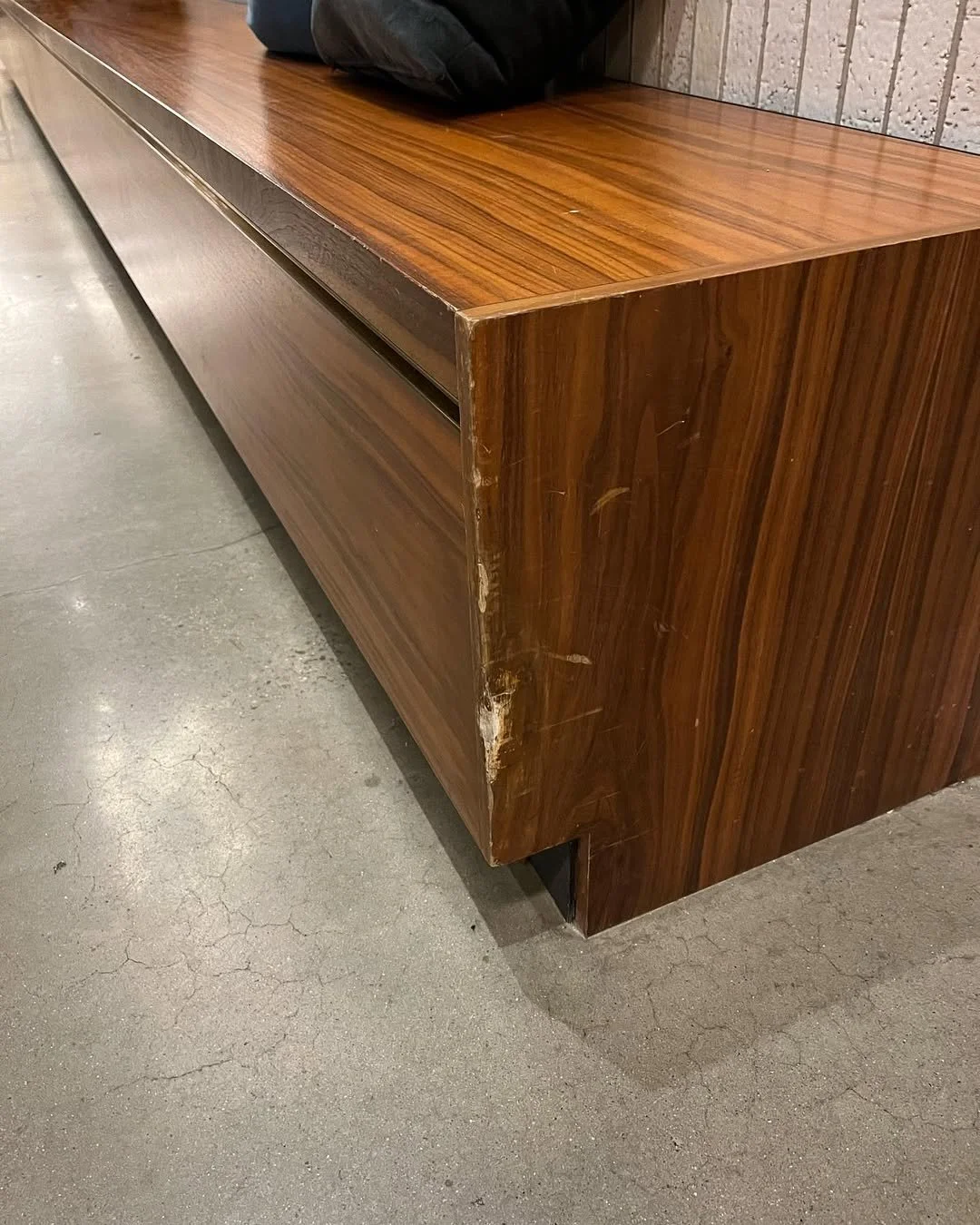 Wooden bench with visible damage and scratches on the corner, placed on concrete floor