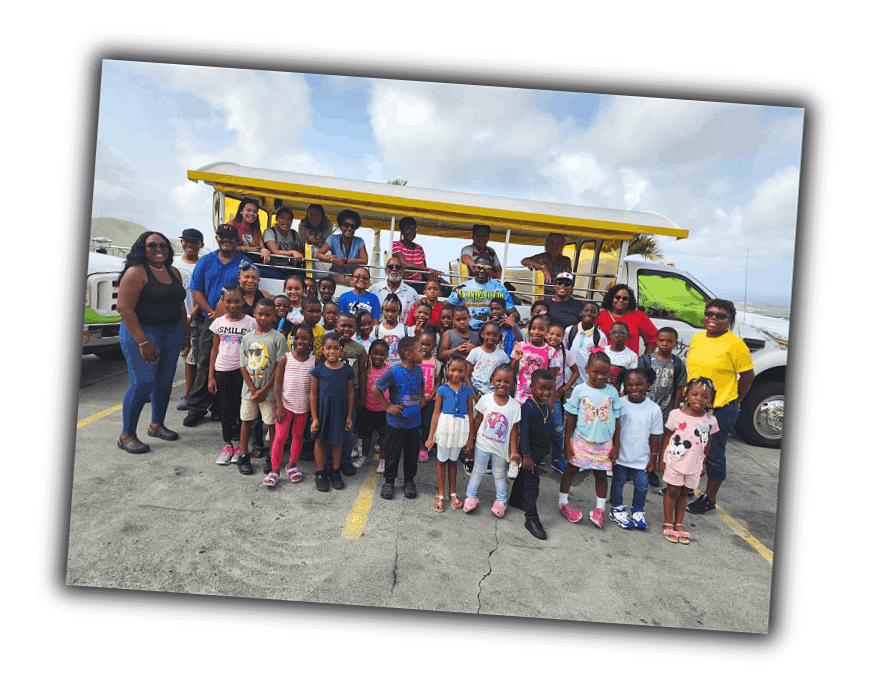 Group of children and adults standing outdoors in front of a tour bus on a partly cloudy day.