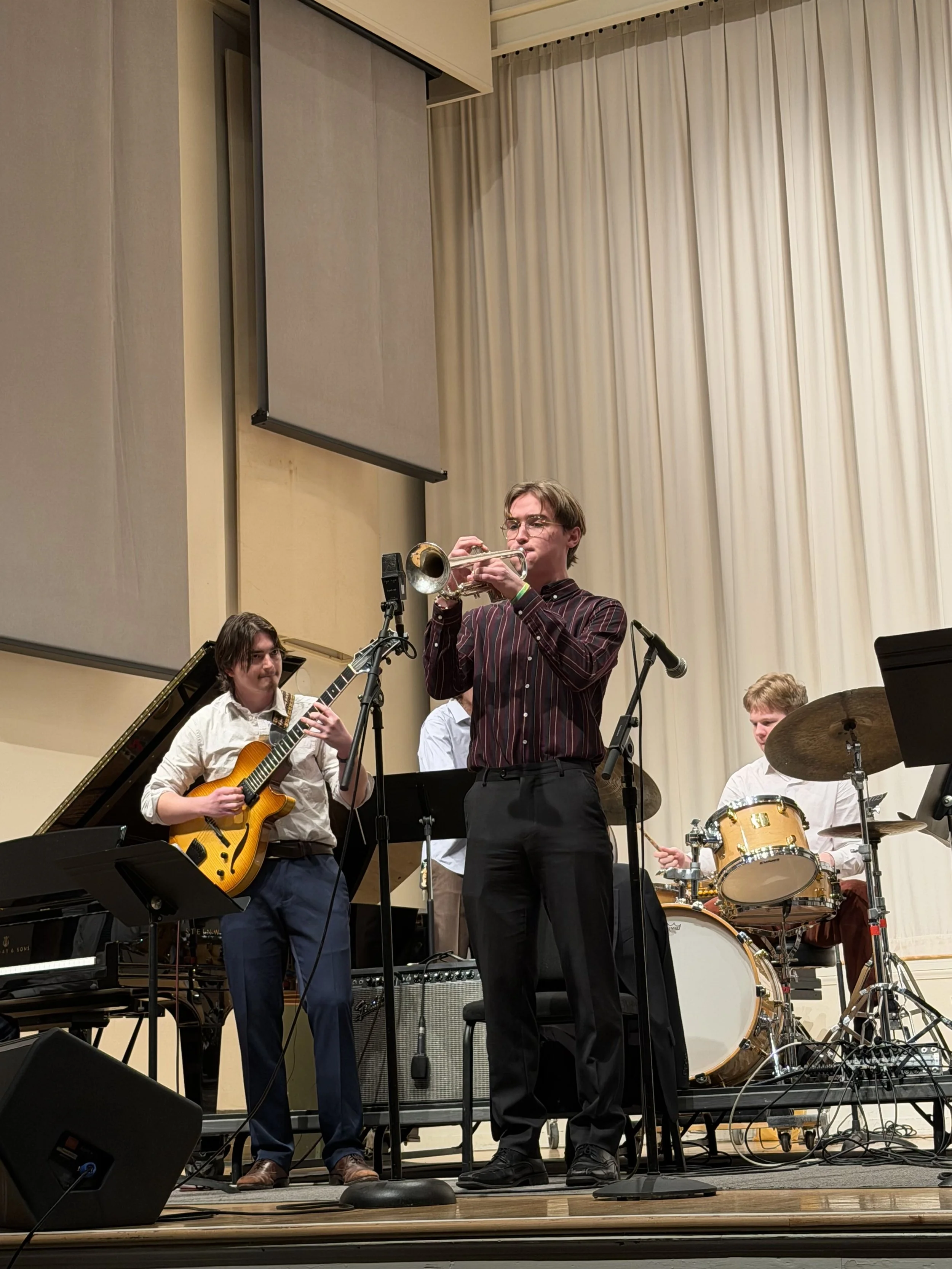 Band performing on stage with a trumpet, guitar, and drums.