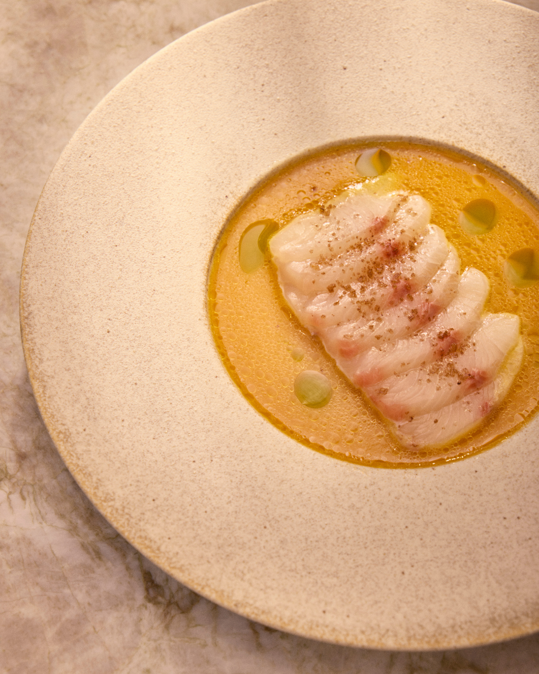 A cocktail glass with a yellow drink and a passion fruit slice on the rim, placed on a table with plates of chips and a bowl of purple chips in the foreground, surrounded by a brown napkin and decorative lantern.