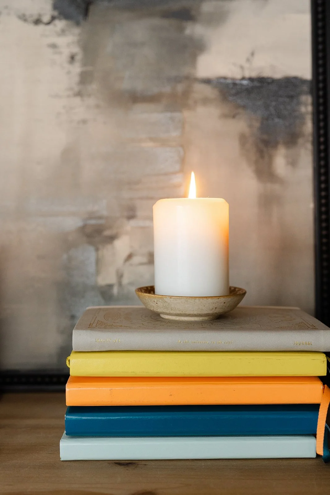 Stack of five colorful notebooks with a burning white candle on top, placed on a wooden surface.