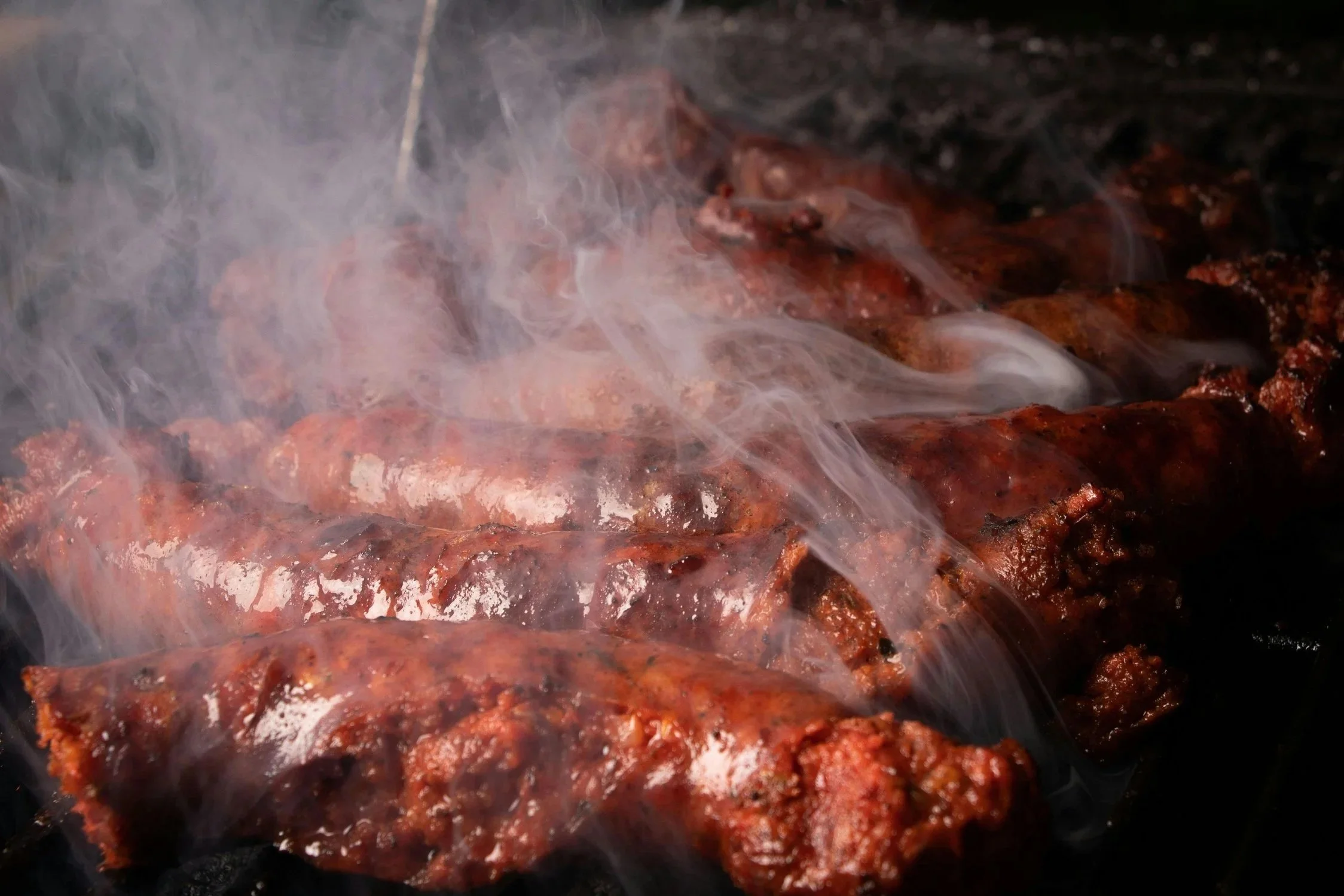 Close-up of racks of marinated meat grilling on an open flame with smoke rising.