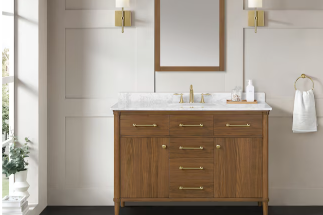 Bathroom vanity with a marble countertop, gold fixtures, and a wooden cabinet, against a light-colored wall with artwork