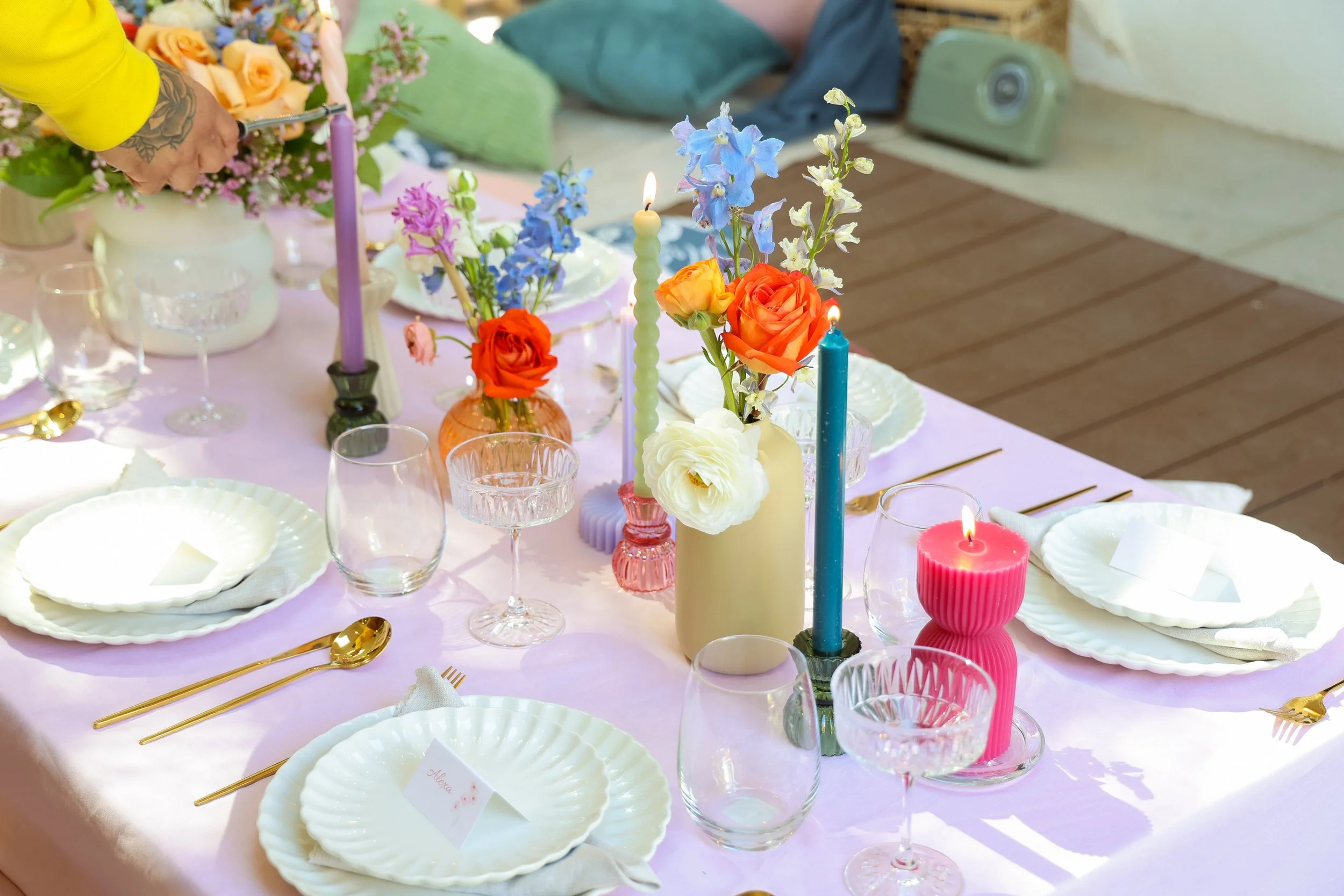 A table decorated with colorful flowers, candles, glassware, and table settings for a celebration or gathering.