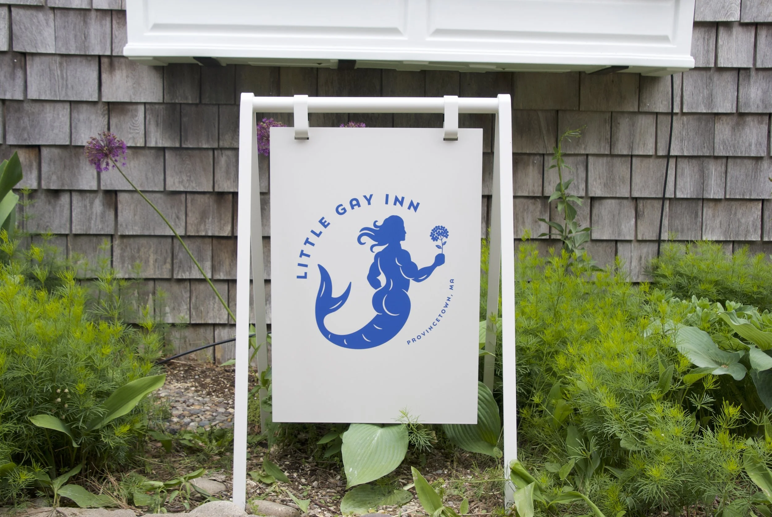 The Little Gay Inn logo, which is a merman with a big butt, holding a hydrangea, on a sign outside the Little Gay Inn.