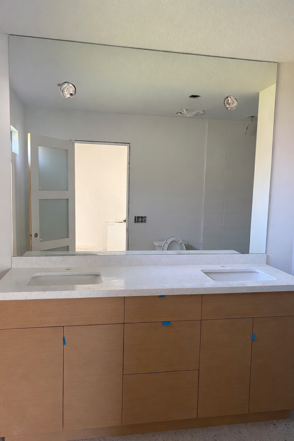 A bathroom under construction with a double vanity mirror and sink, a partially finished shower area, and a door leading to another room.
