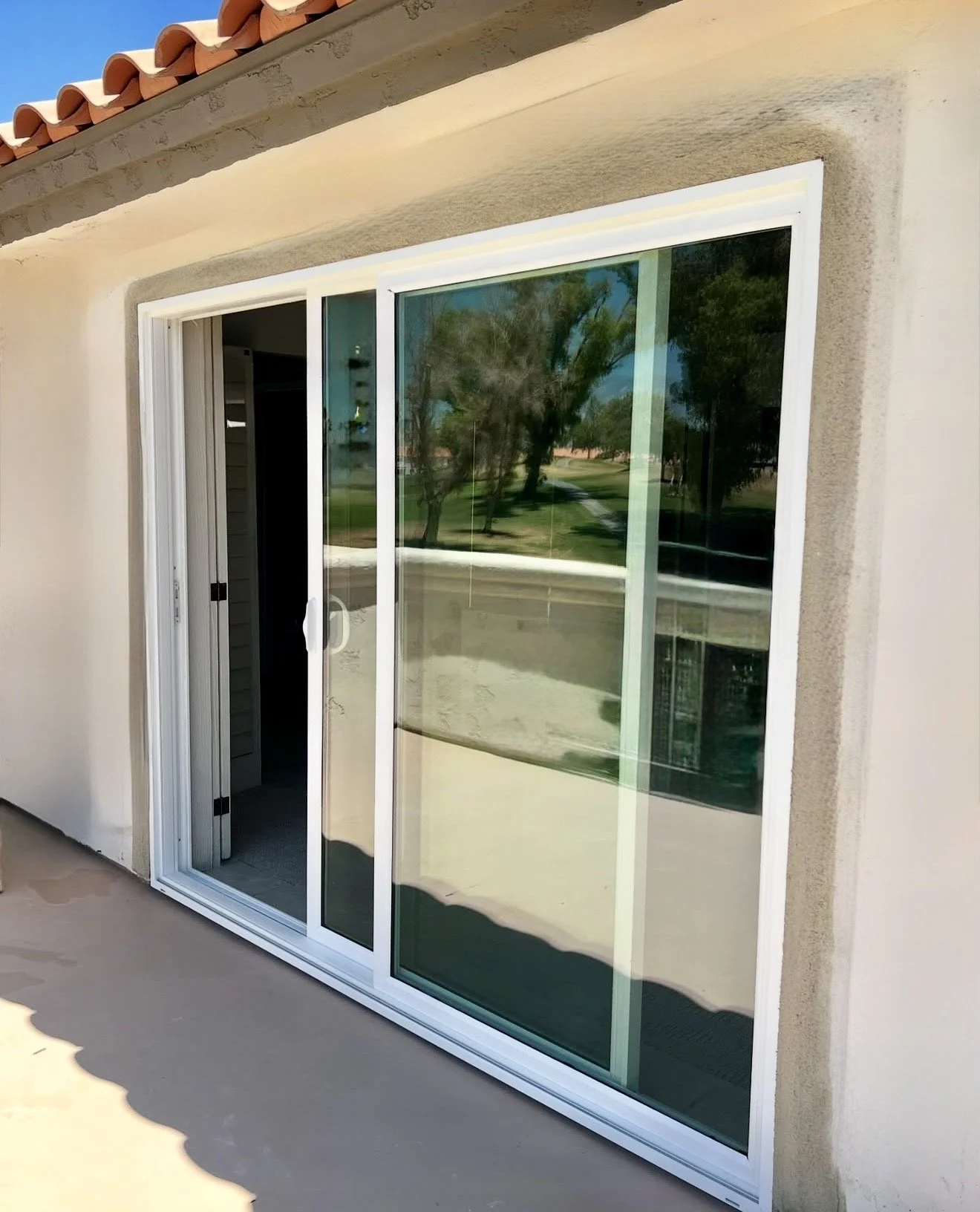A sliding glass door leading into a house, with a reflection of trees and a pathway outside, and a tiled roof above.