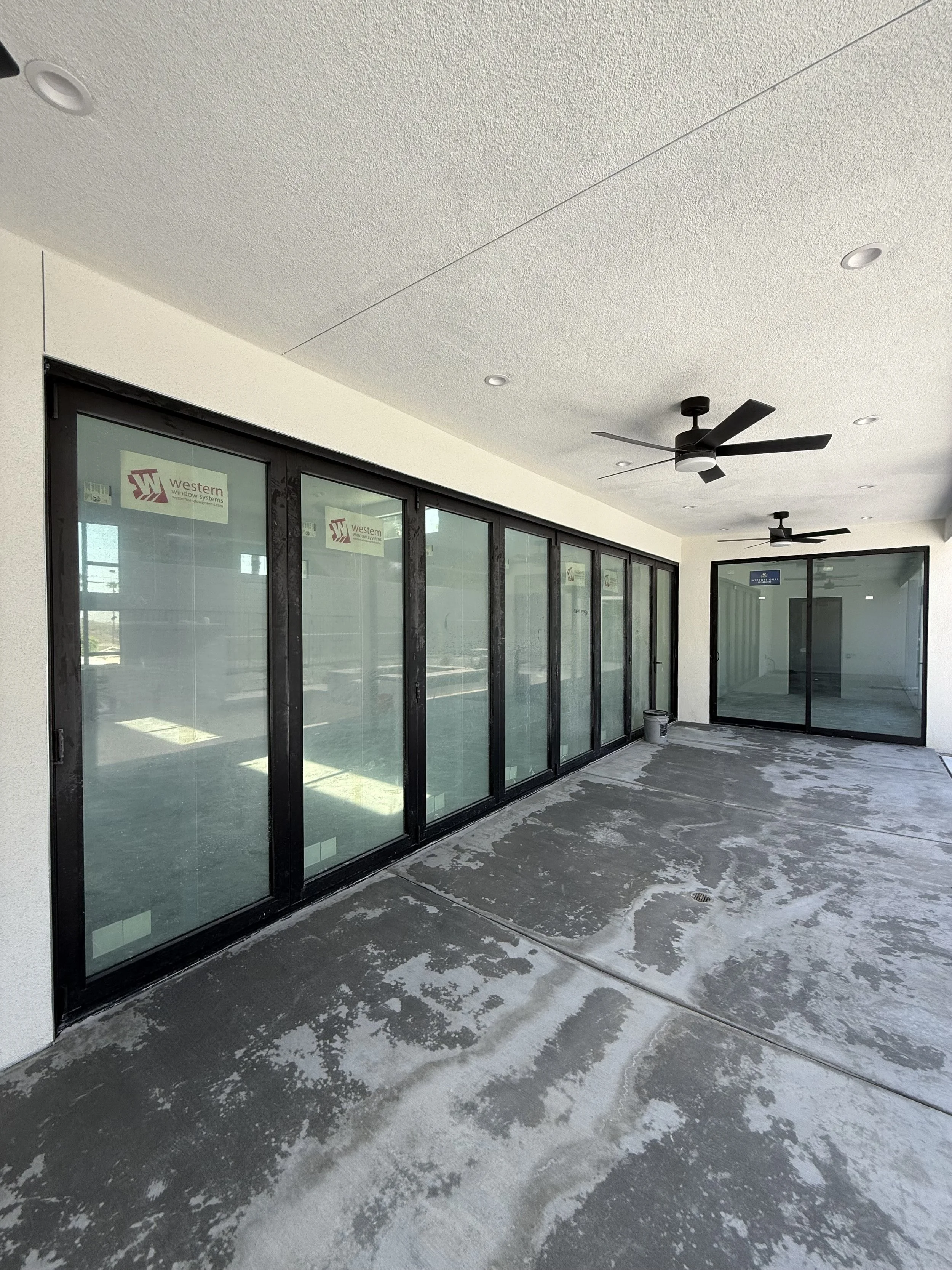 Covered outdoor patio with sliding glass doors, ceiling fans, and an unfinished concrete floor.