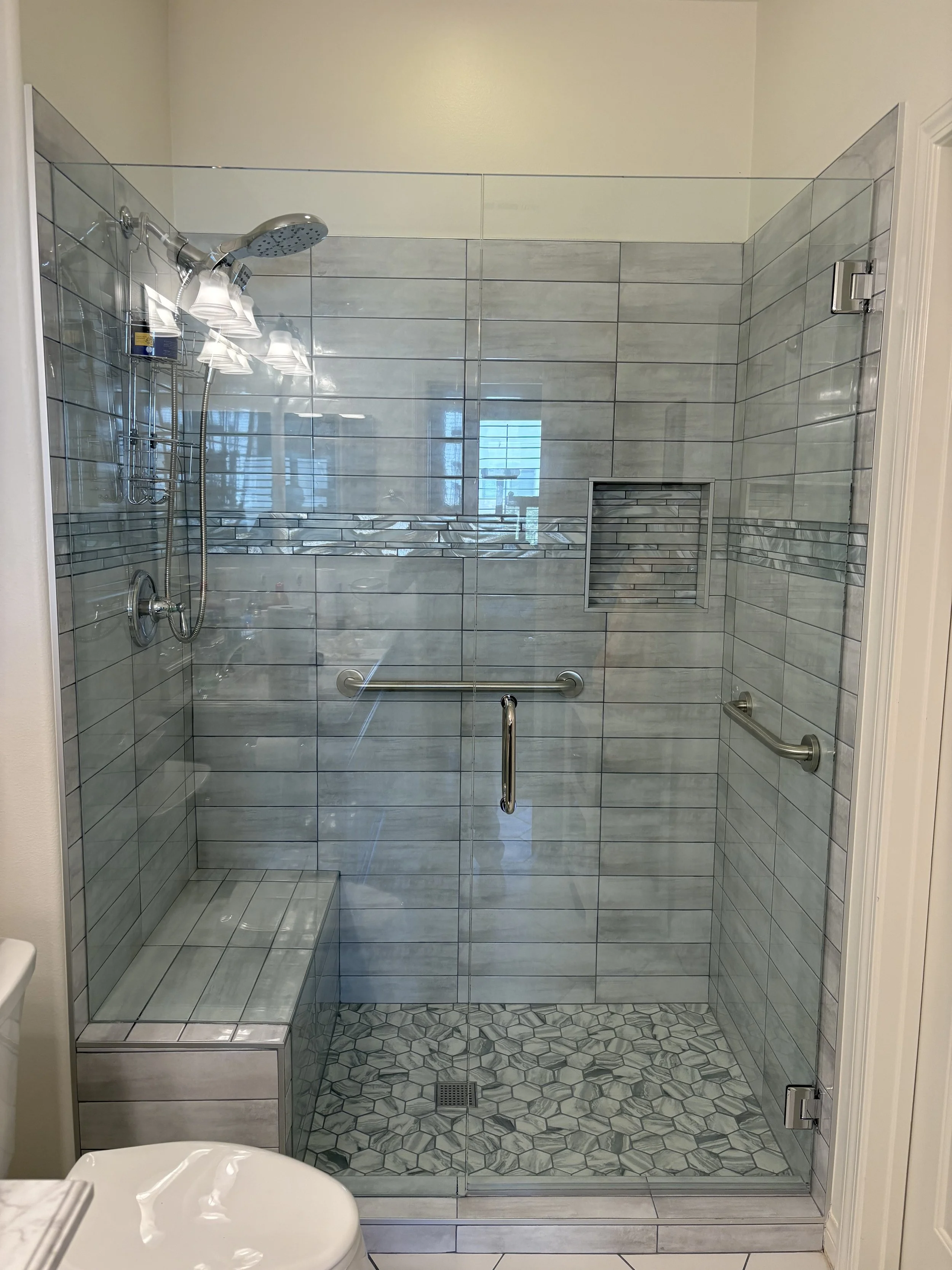 Glass shower enclosure with a bench, tile walls, a built-in niche, and a rain showerhead.