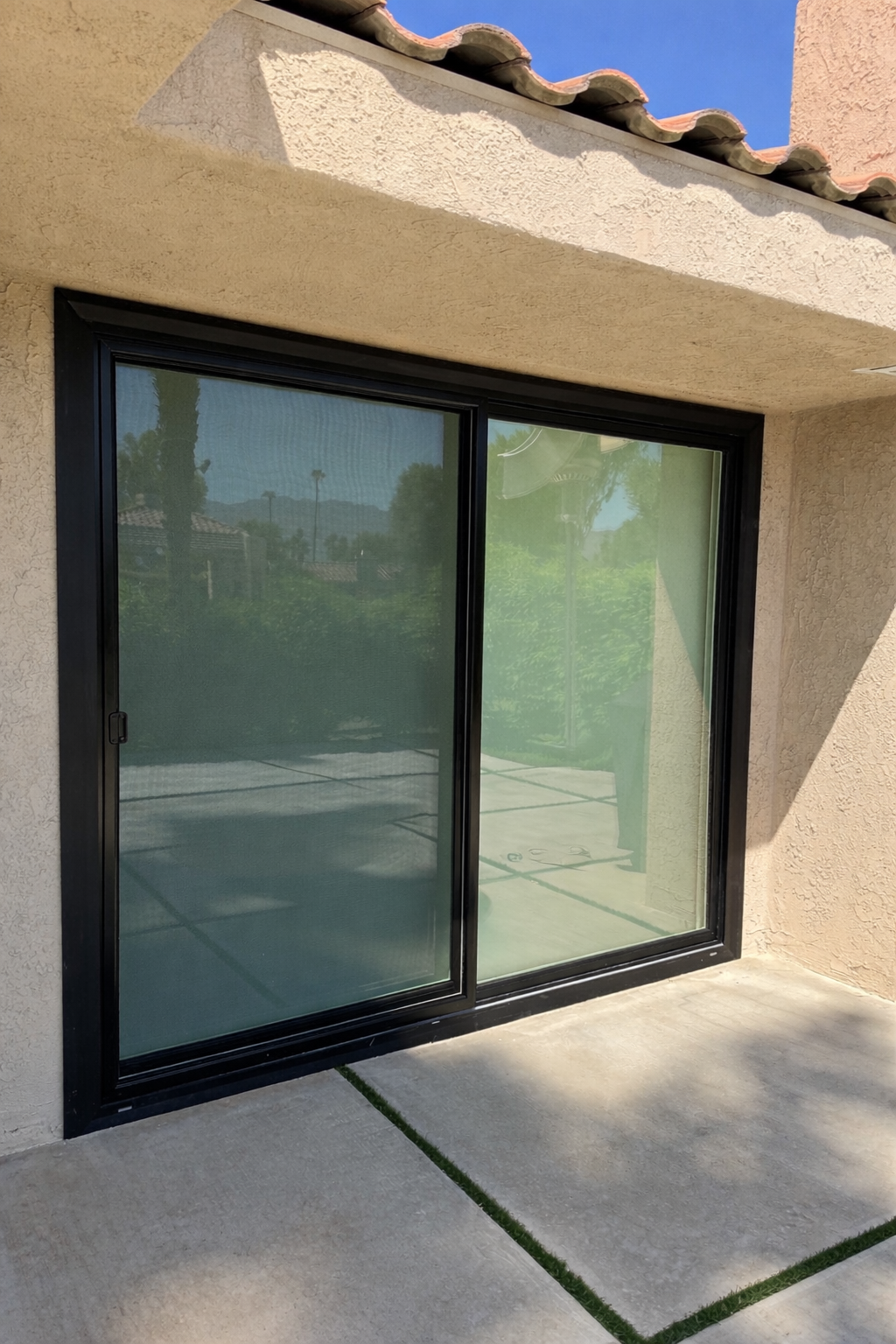 A sliding glass door with black frame on an outdoor patio, with a screen door on the left side and reflection of trees and sky in the glass