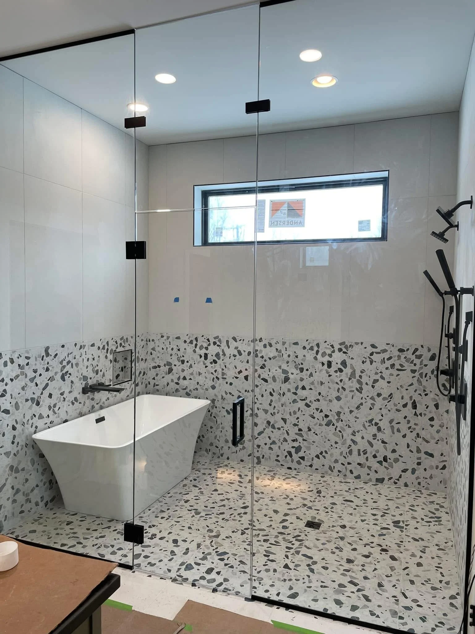 Modern bathroom with a freestanding bathtub, a large shower area with pebble tiles, a horizontal window, and black fixtures.