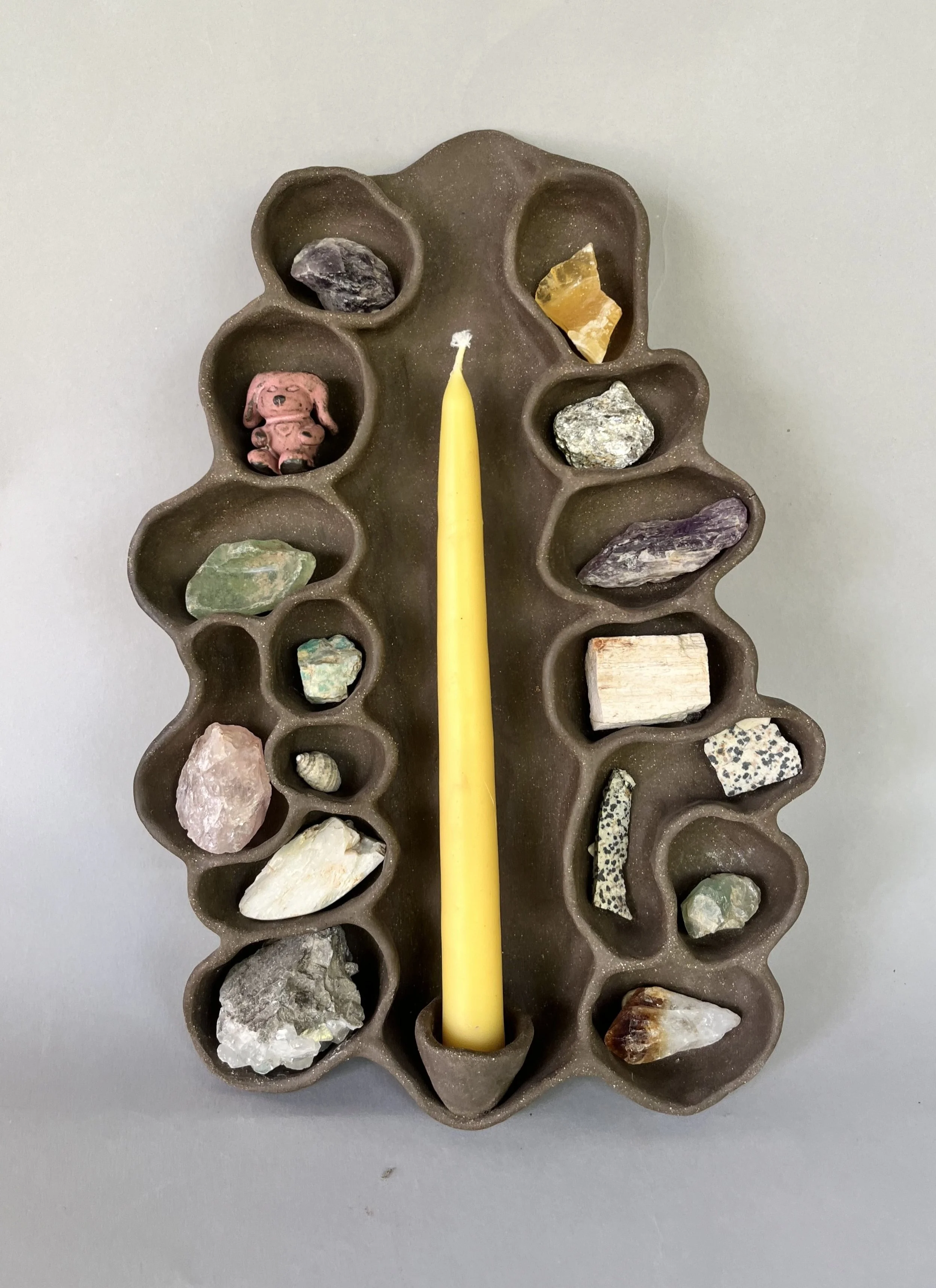 A brown candleholder with multiple compartments holding various colorful rocks and a yellow candle in the center.