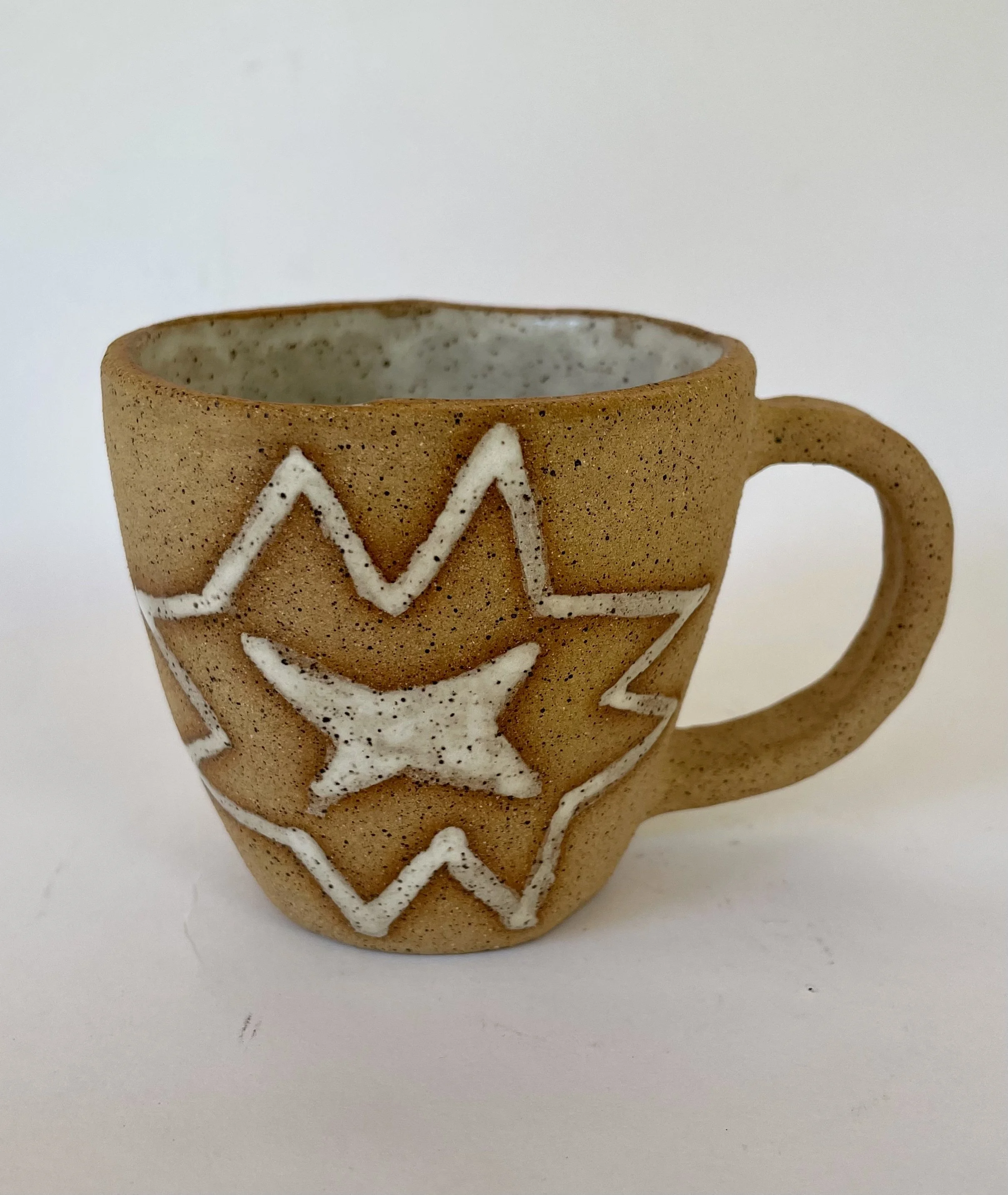 A ceramic mug with a quilt star design on it, beige in color with white decorative lines.