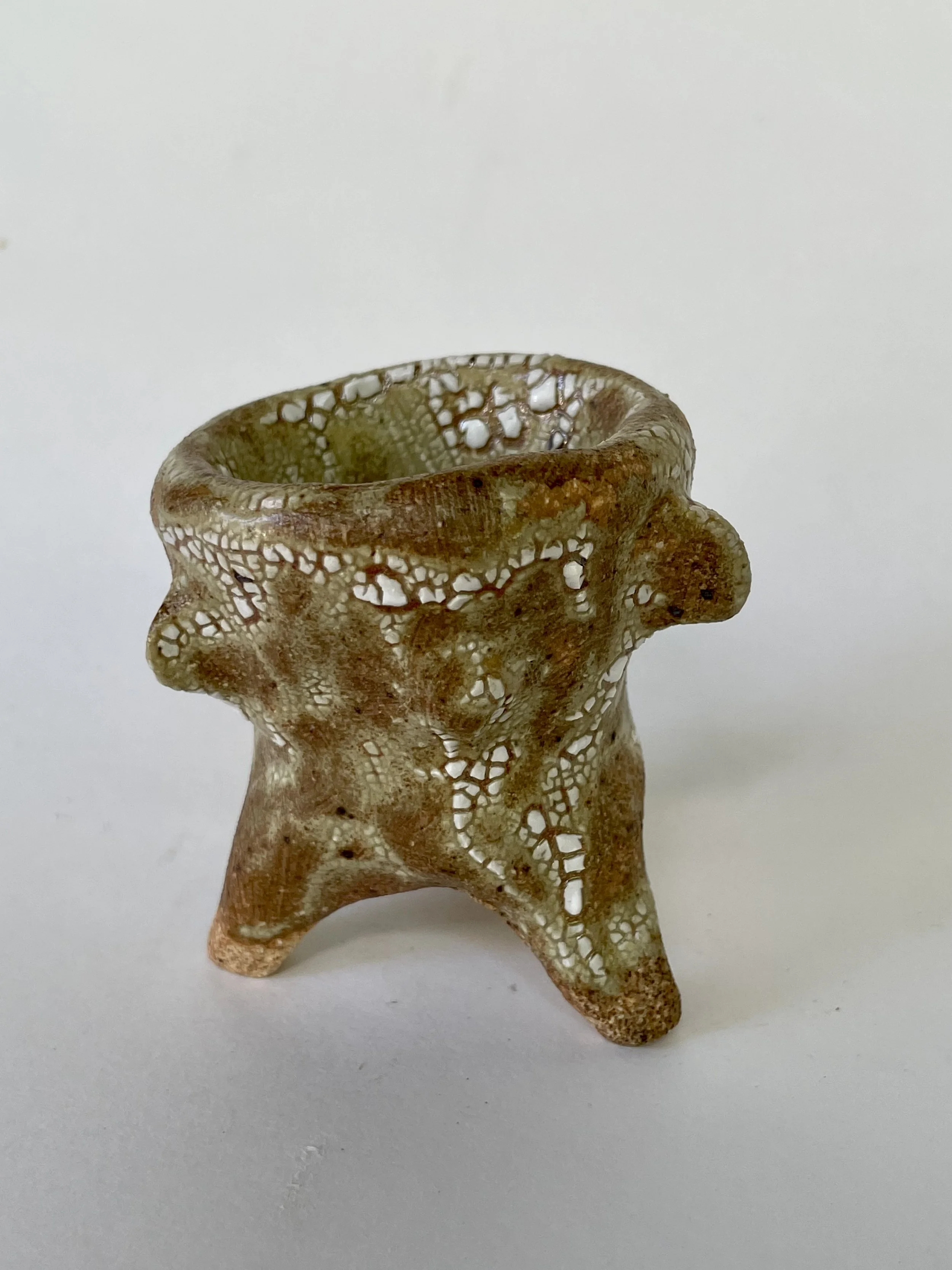 A small sculpture with a porous, web-like design and three legs.