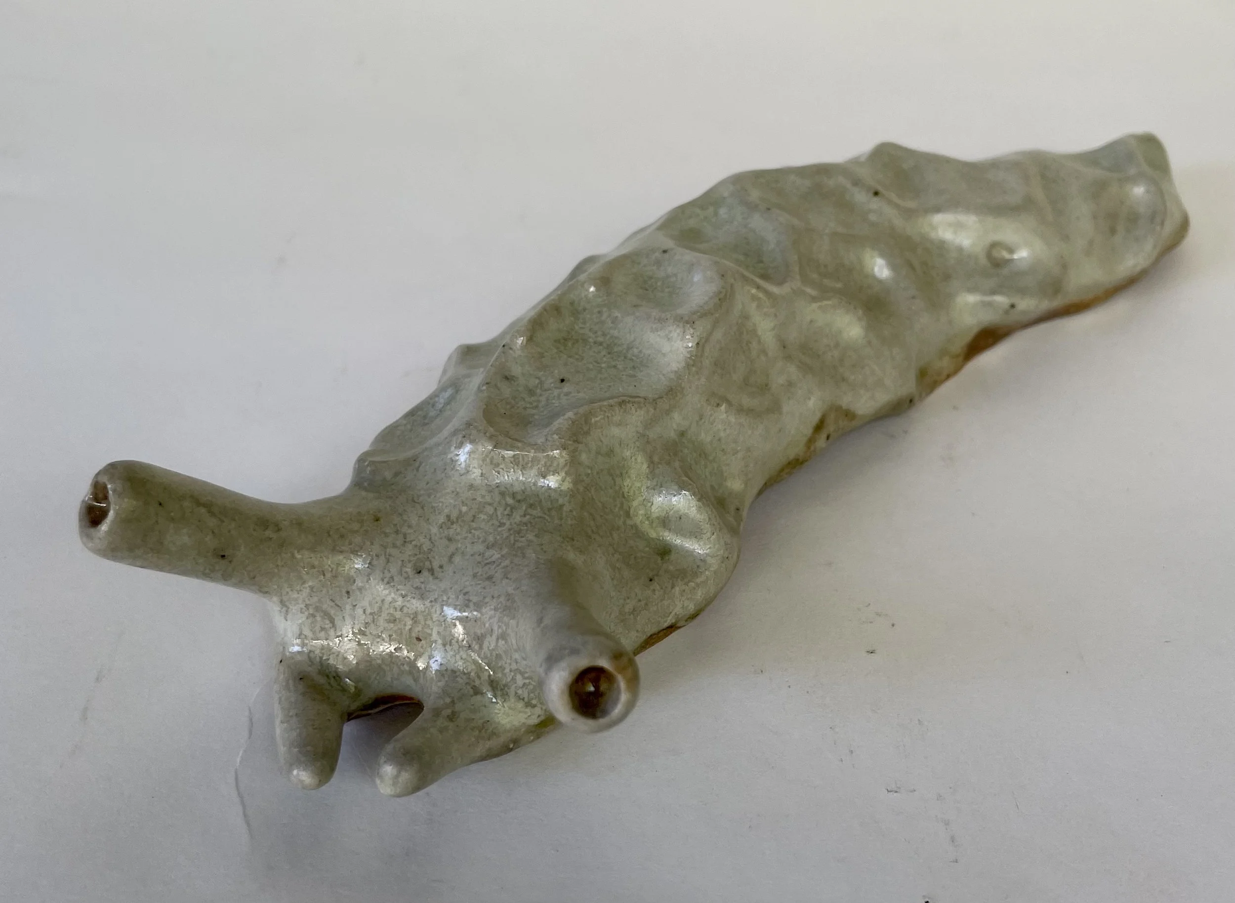 A ceramic or porcelain slug figurine lying on a white surface.