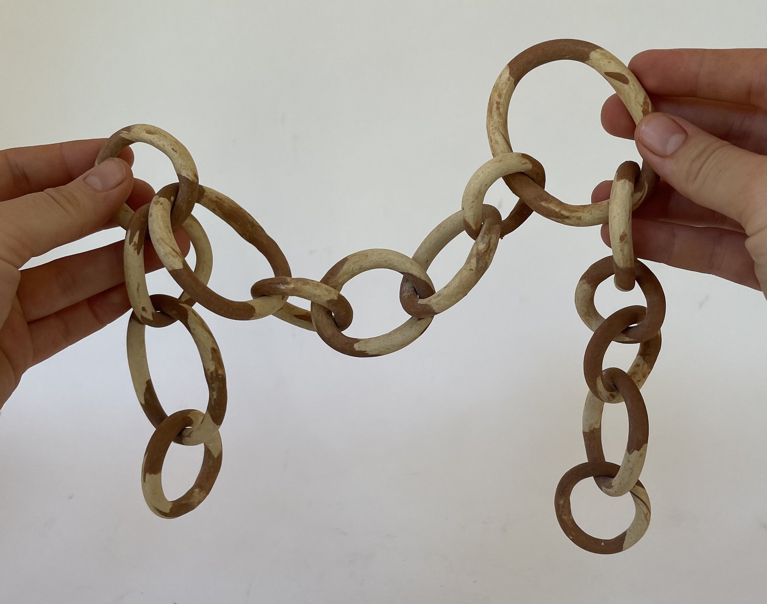 Two hands holding an interlinked chain of ceramic rings against a plain white background.
