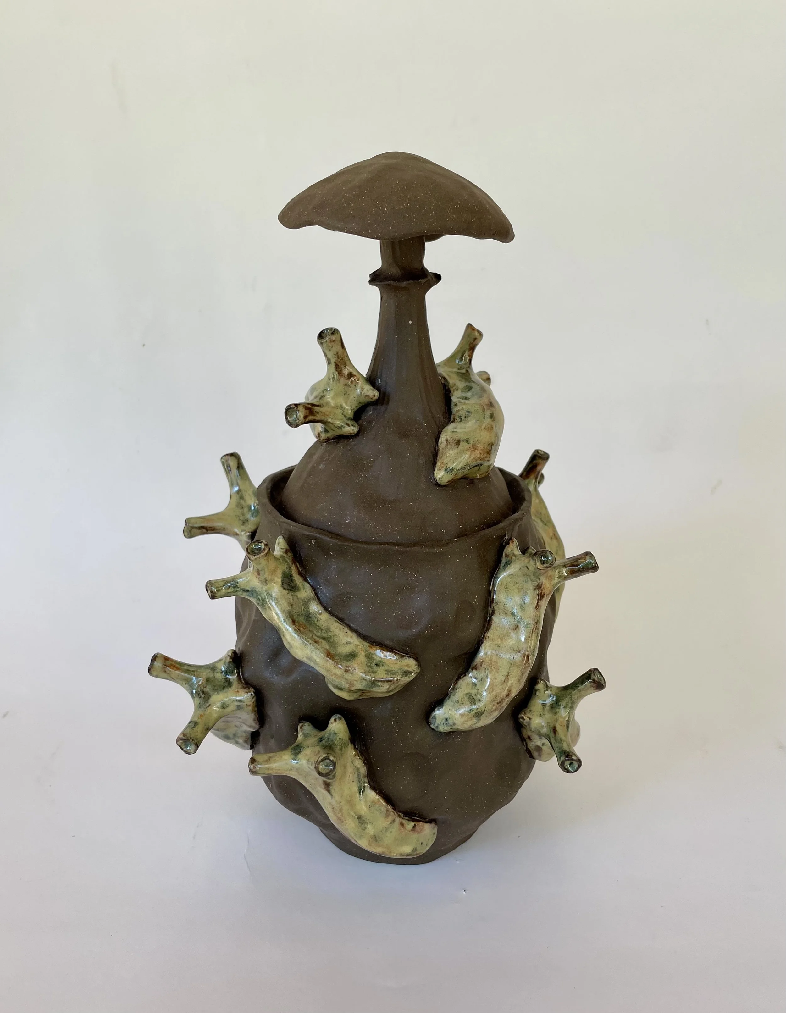 A ceramic sculpture resembling a mushroom with slugs crawling upward, featuring a large mushroom cap on top and a rounded base, with beige and brown colors and textured details.
