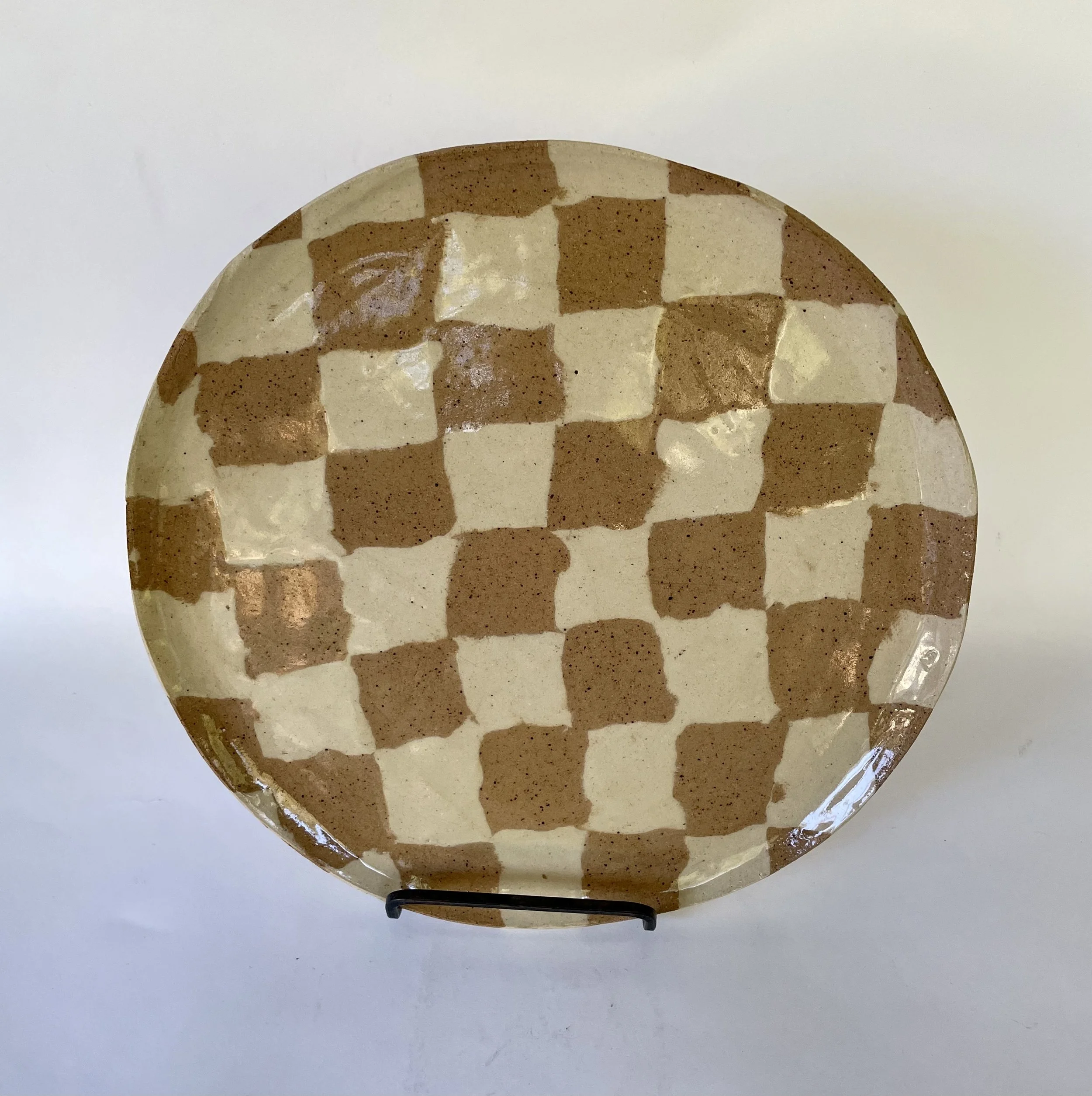 Round ceramic plate with a checkerboard pattern of brown and beige squares, placed on a white surface.