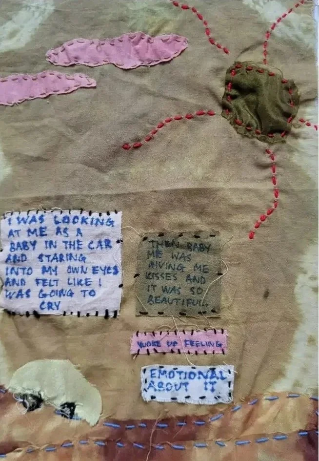 Crafted fabric pieces with handwritten messages on a textured background, including pink, cream, and beige cloth with colorful thread embroidery and red dotted lines.