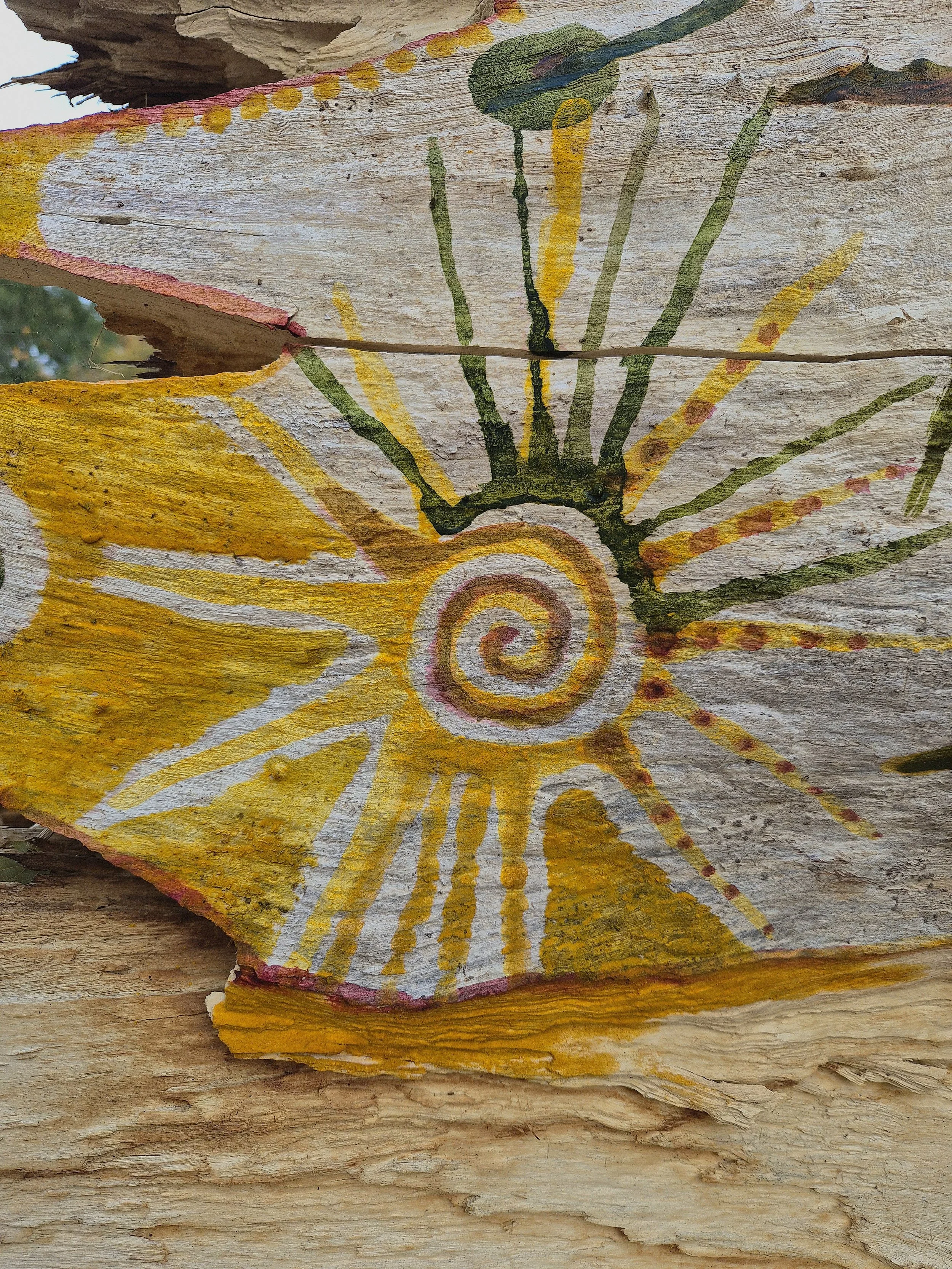 Colorful hand-painted spiral and sunburst design on weathered wood slice.