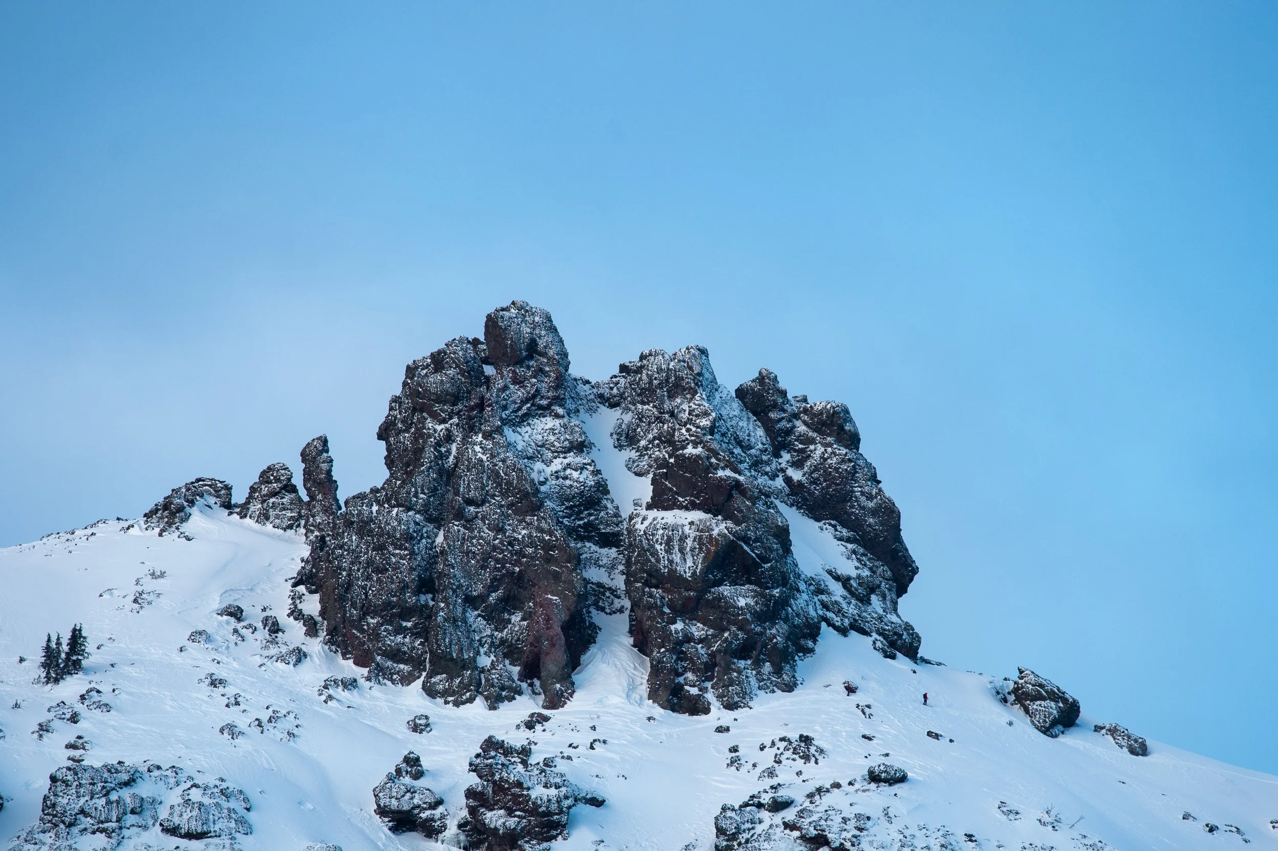Snow-covered mountain with dark rocky formations and a light blue sky