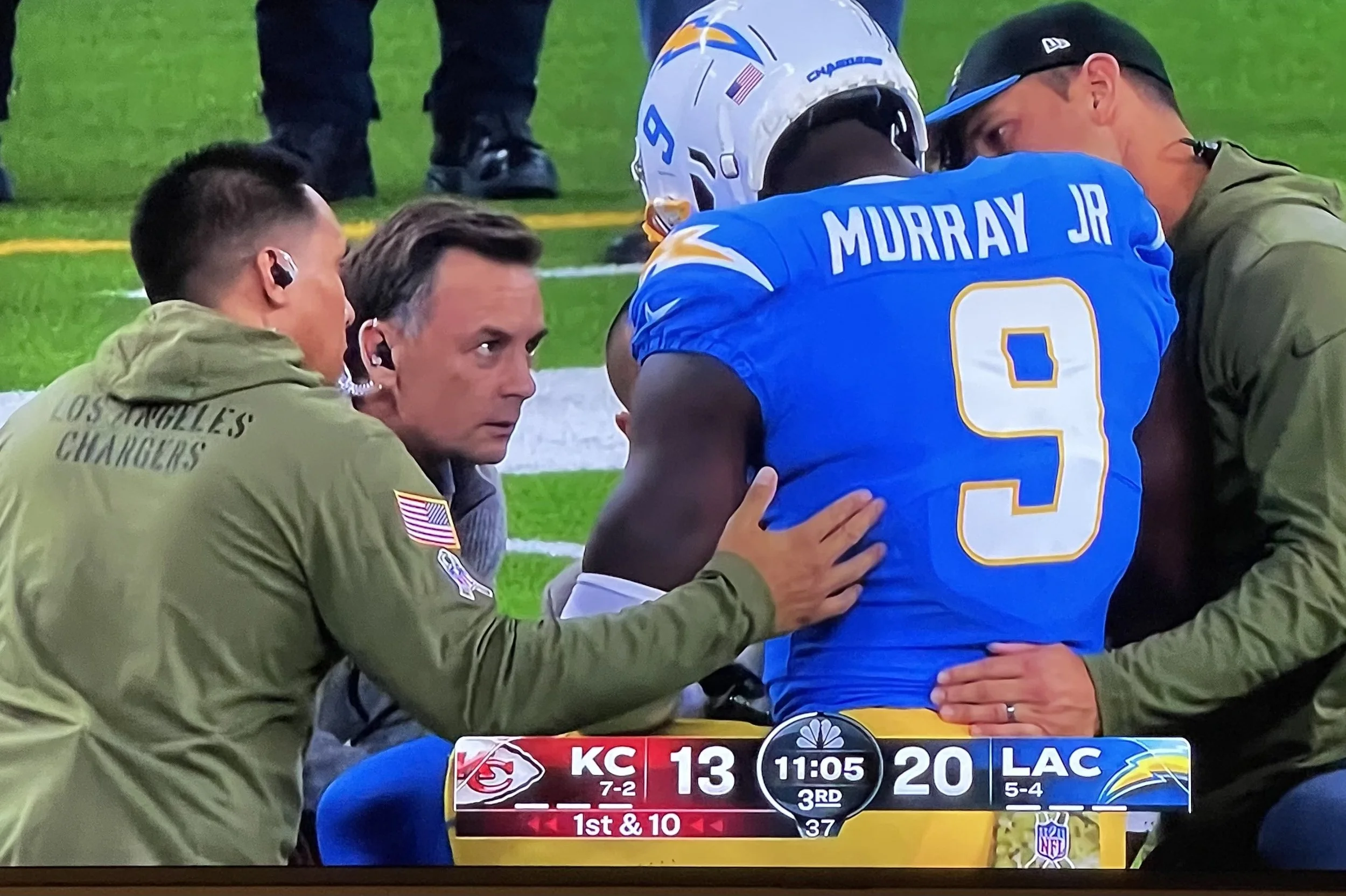 Two football players and two medical staff members are gathered on the sideline during a game. One player, wearing a blue jersey with the number 9 and the name Murray Jr, is sitting on the bench. The other person wearing a green jacket has the words 'Los Angeles Chargers' on it. The game score shows Kansas City Chiefs 13, Los Angeles Chargers 20, with 11 minutes and 5 seconds left in the third quarter.