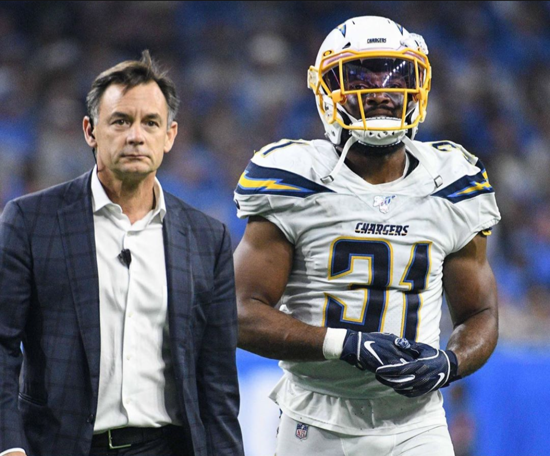 A Los Angeles Chargers football player in a Los Angeles Chargers uniform and helmet stands next to Dr. Russell Petrie in a suit on a football field.