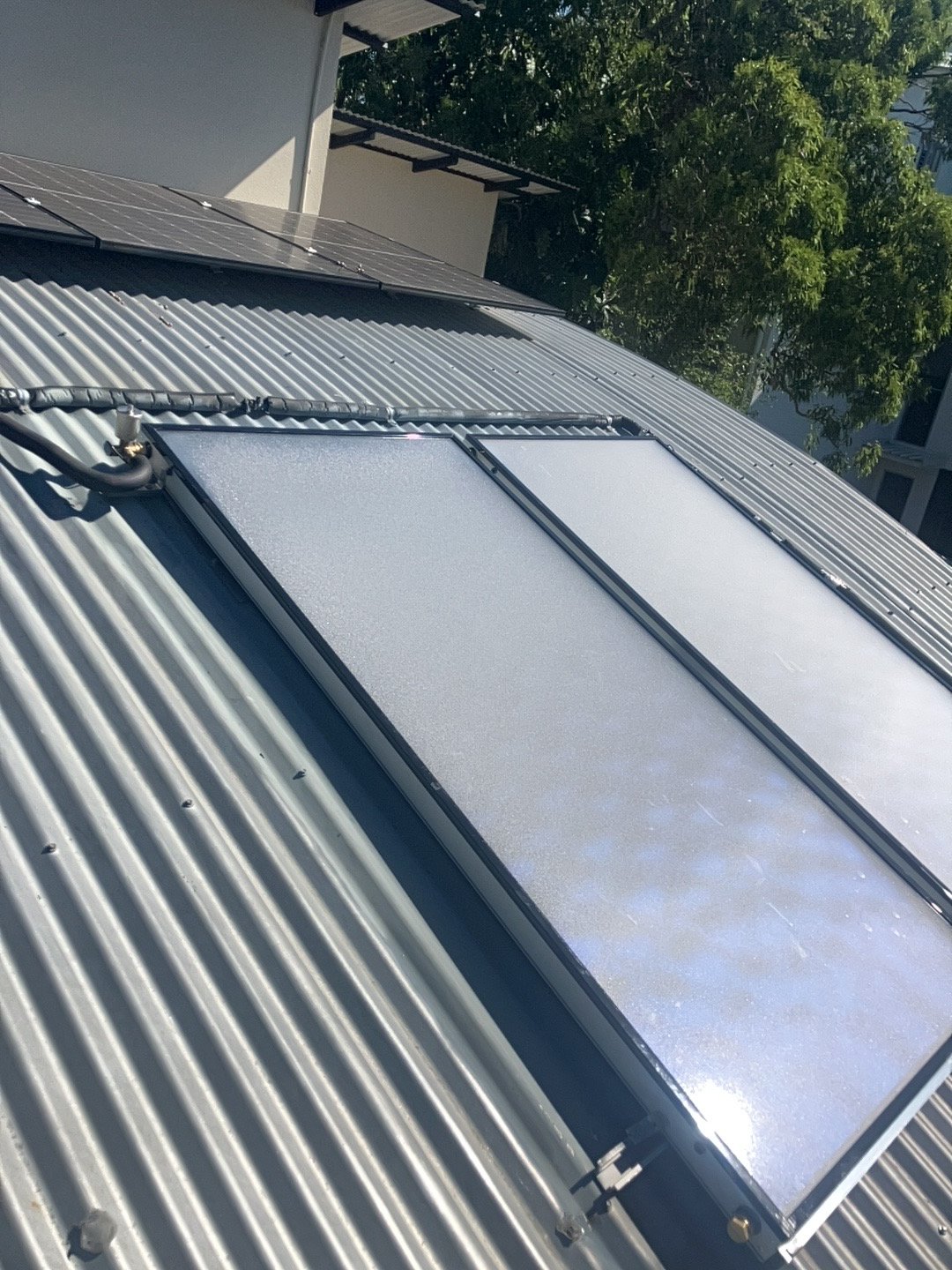 Close-up of a solar water heater installed on a metal roof, with solar panels and a cylindrical tank visible.