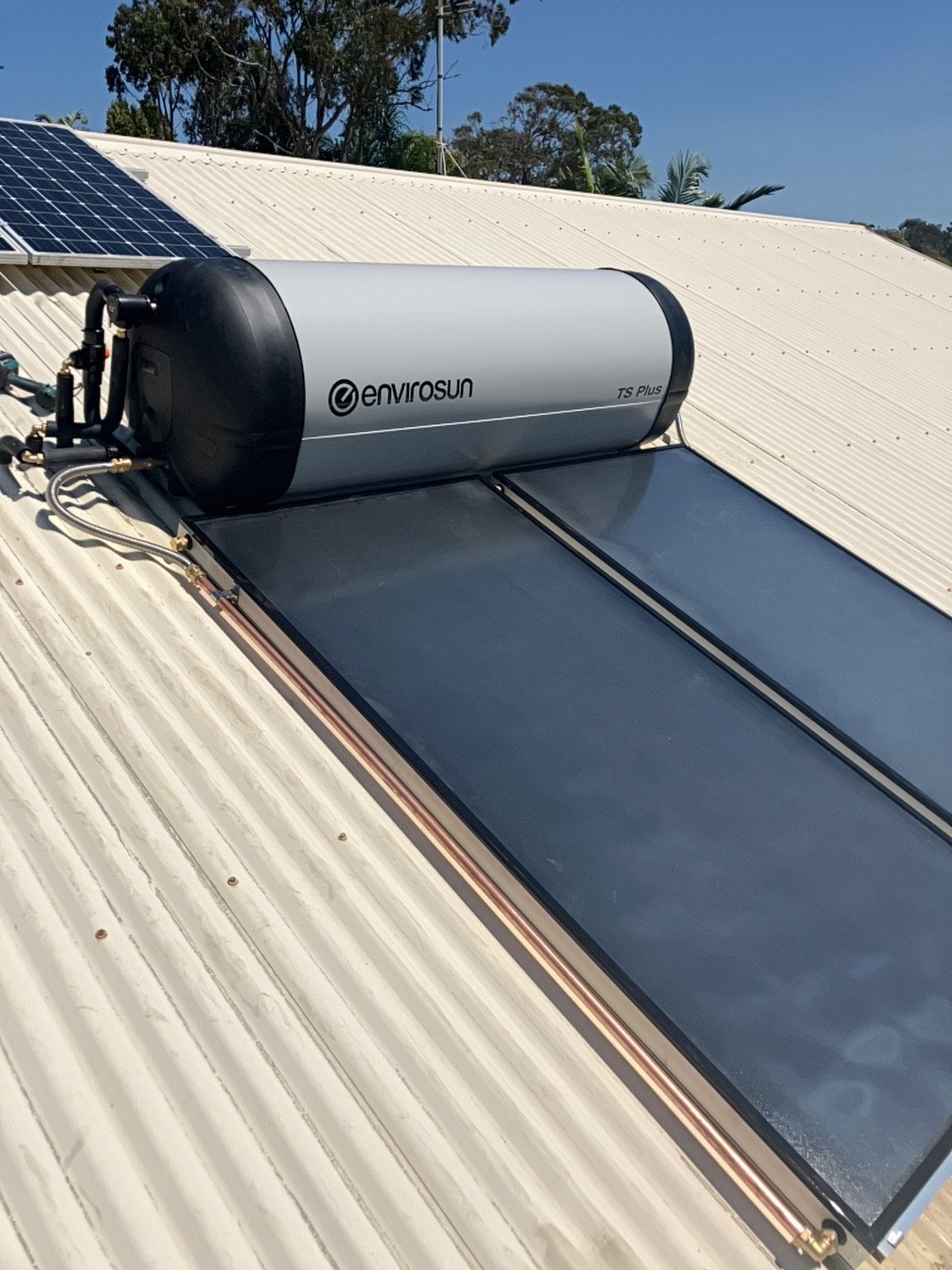 A solar water heater system installed on a rooftop, including solar panels and a water storage tank labeled 'EnviroSun TS Plus'.