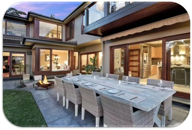 Outdoor dining table with eight chairs in backyard of modern house with large windows and patio area