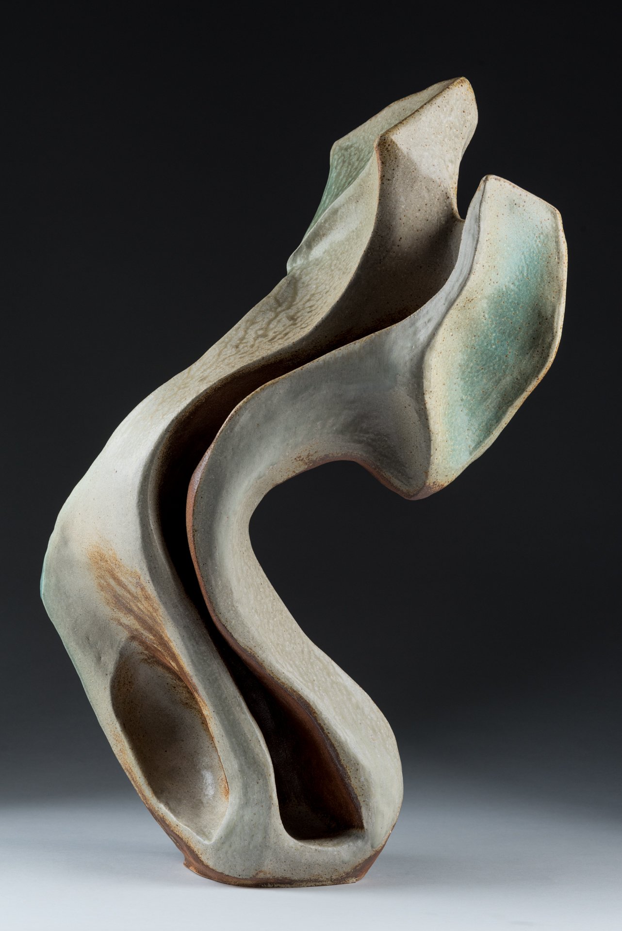 Abstract ceramic sculpture of a dancer with flowing, curved shapes and earthy colors against a black background.