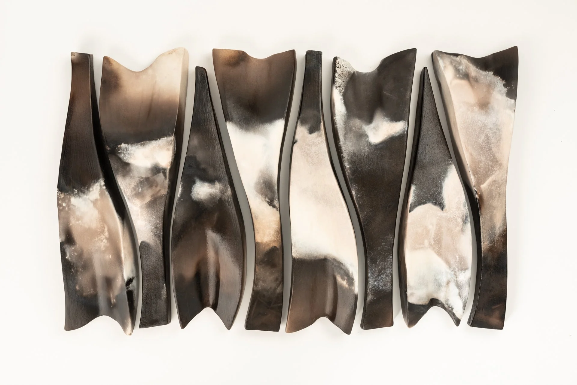 Abstract ceramic wall art with black, beige, and white pit-fired forms arranged vertically on a white background.
