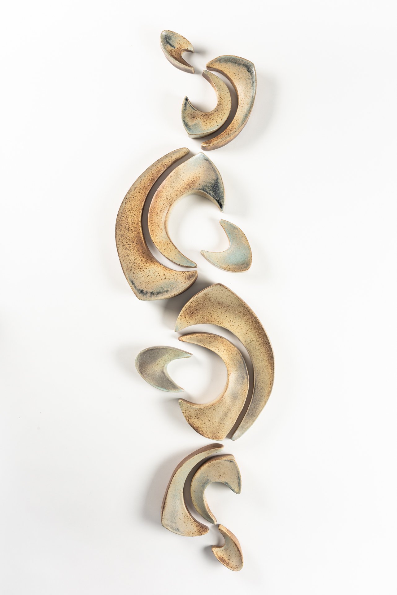 Abstract ceramic sculpture pieces arranged vertically on a white background.