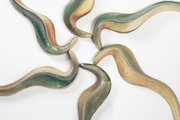 Close up view of 18-part abstract wall sculpture in which 6 curvy serpentine shapes are arranged in a circle with their heads touching