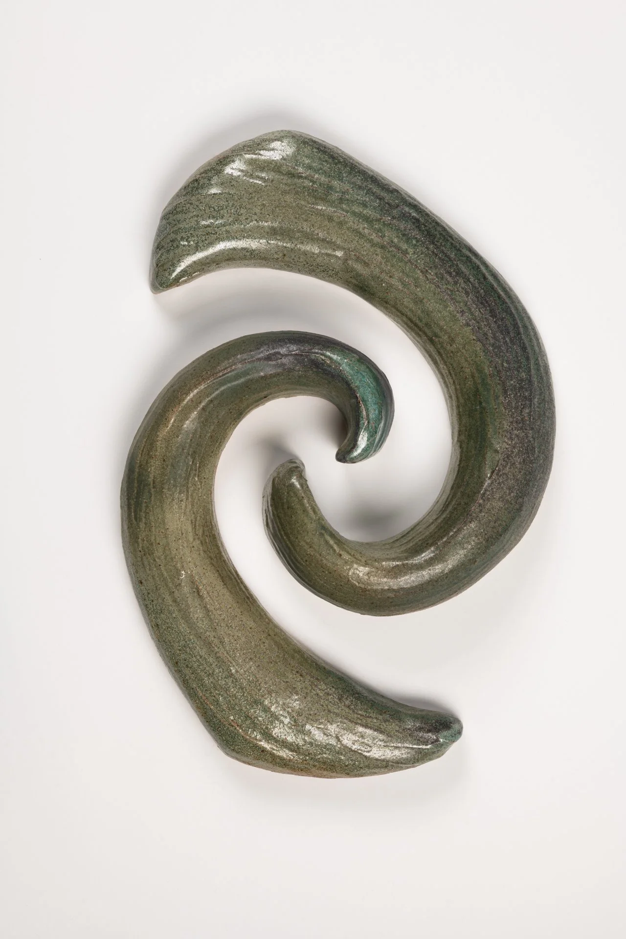 A wall sculpture featuring two large, curved, greenish-brown ceramic pieces arranged in a swirl on a white background.