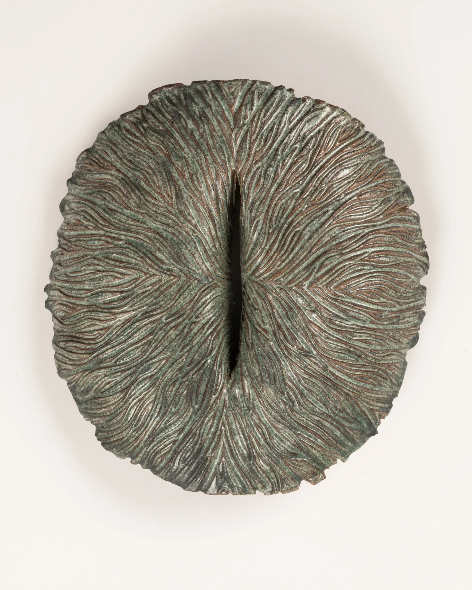 Ceramic oval-shaped wall sculpture with green glaze and intricate carved line patterns on a white background.
